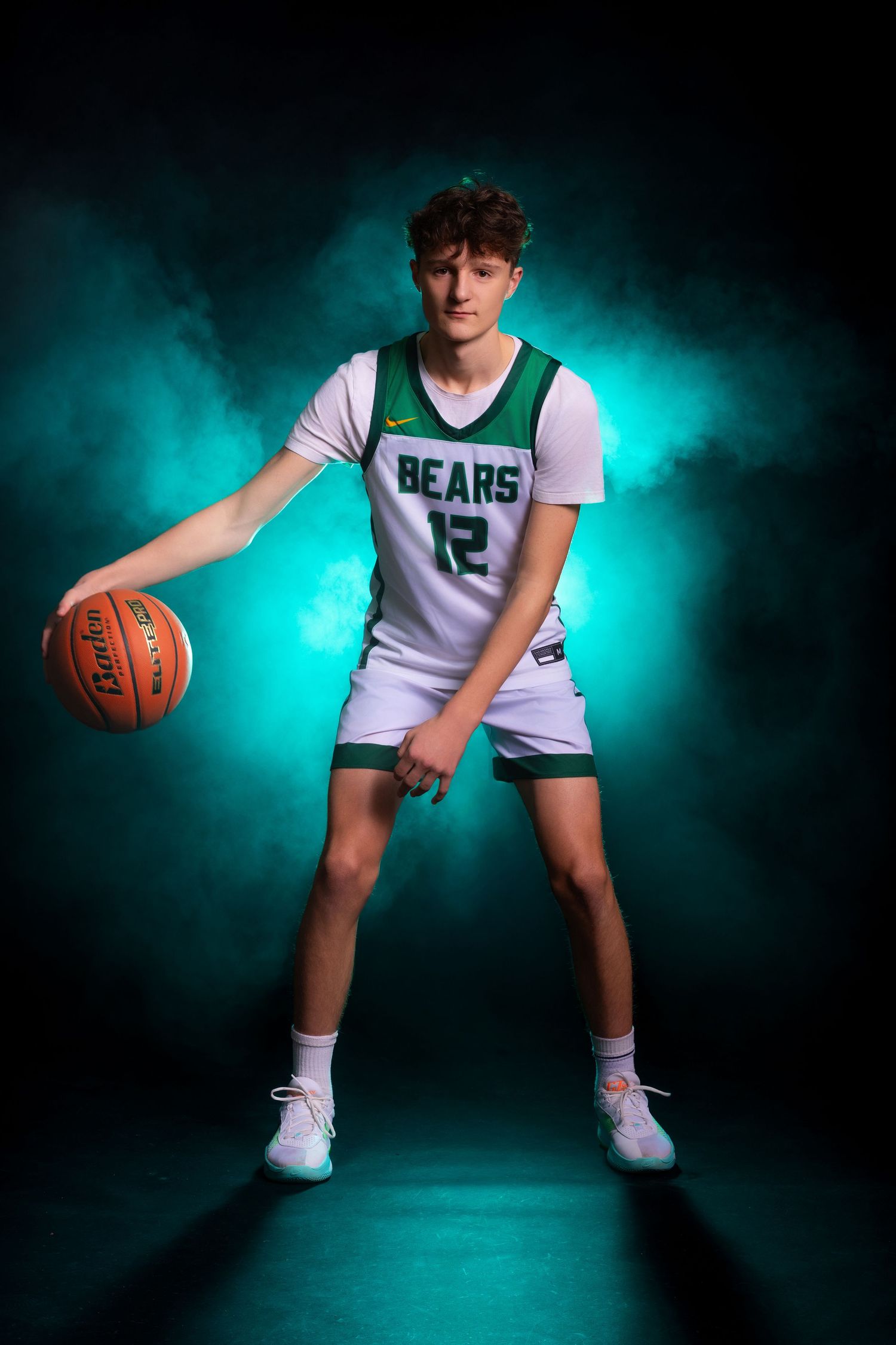 Basketball player in white Bears jersey poses with ball against dramatic teal backdrop in professional sports photoshoot.