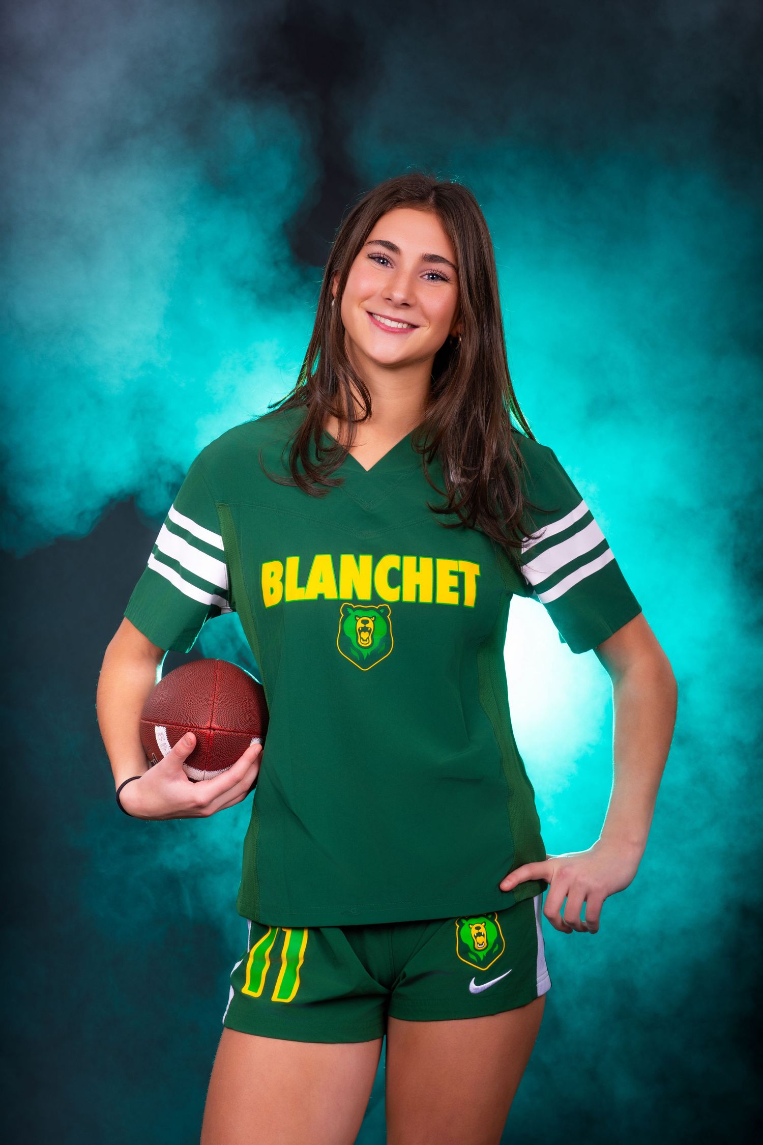 Athlete in green Blanchet sports uniform holds football while posing against turquoise smoky background.