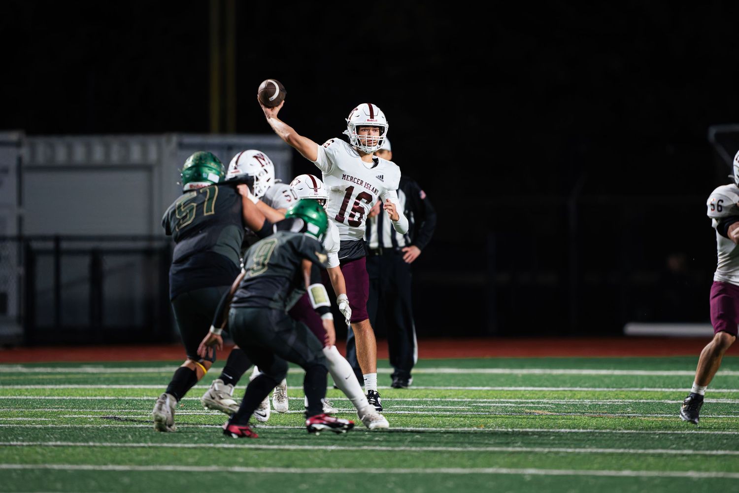 Football players engage in a play during a nighttime game on an illuminated field with artificial turf.