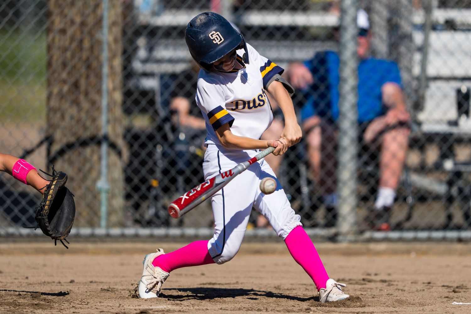 Action sequence of a softball player at bat making contact with the ball during a game.