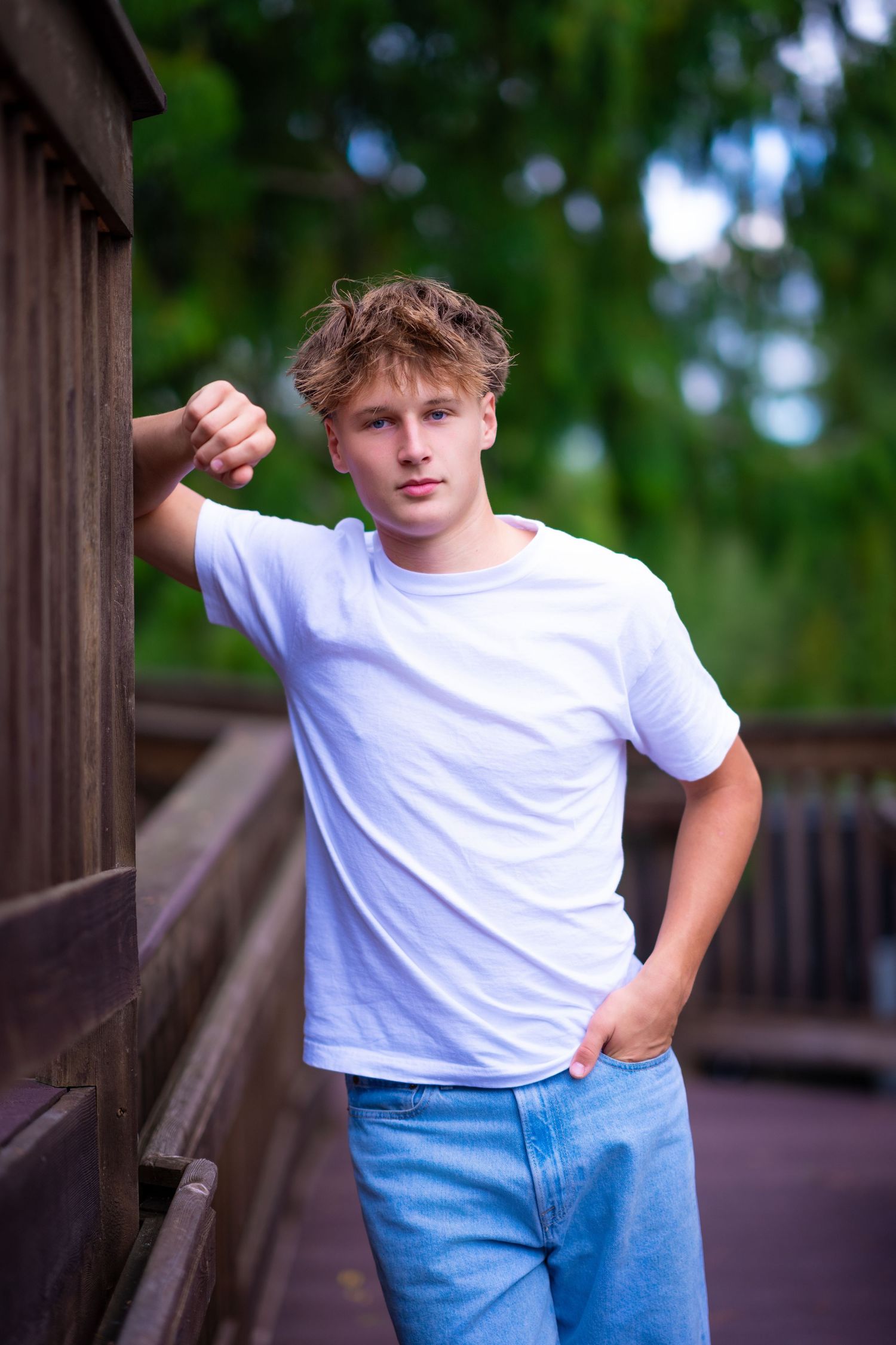 Casual portrait of person in white t-shirt leaning against wooden railing outdoors.