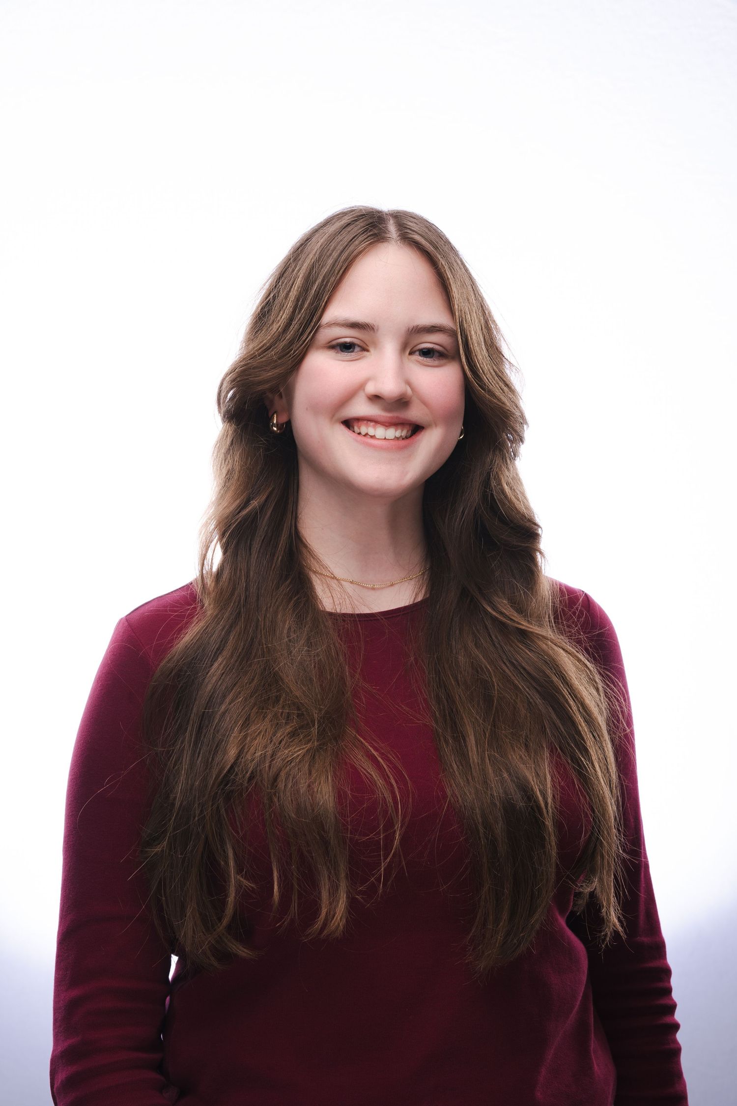 A person with long brown hair wearing a burgundy sweater smiles warmly against a white background.
