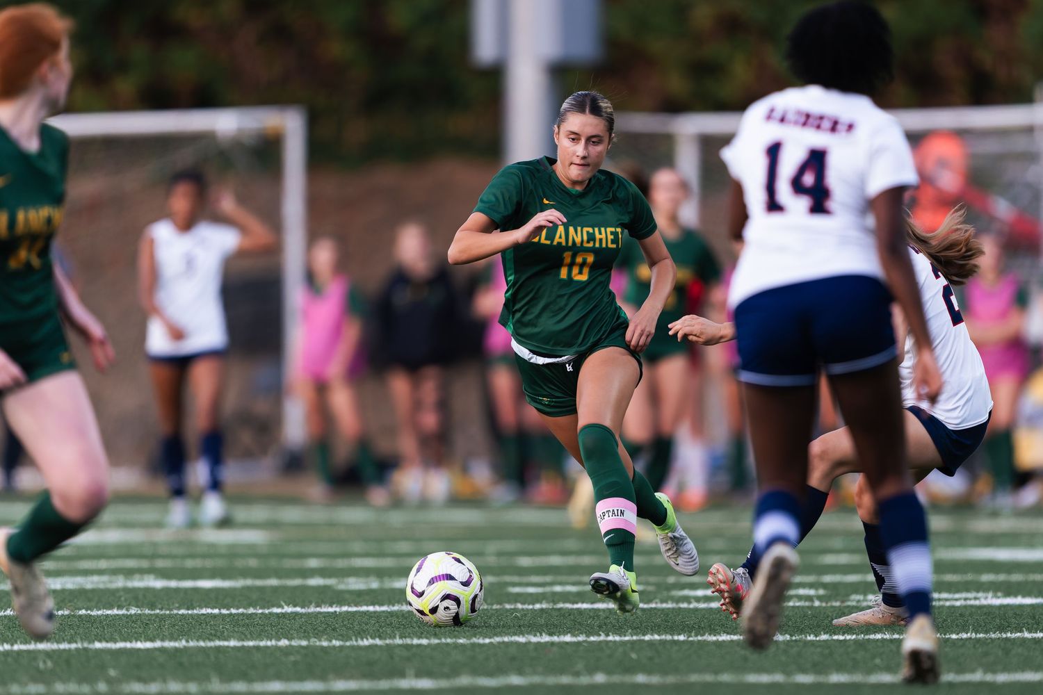 Soccer player in green jersey slides to block the ball during an intense match on artificial turf.