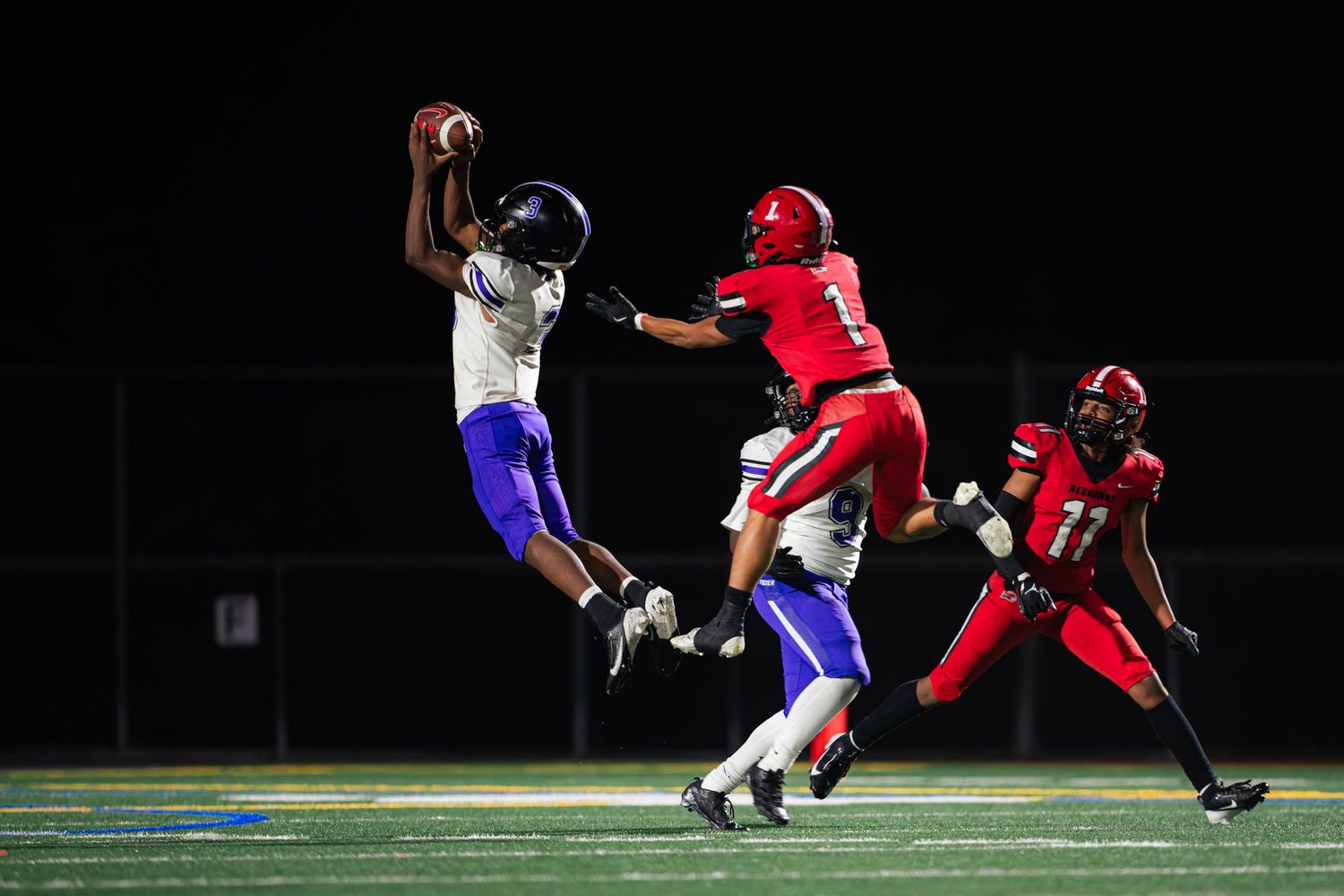 Football players in red and blue uniforms compete in a nighttime game on an illuminated field.