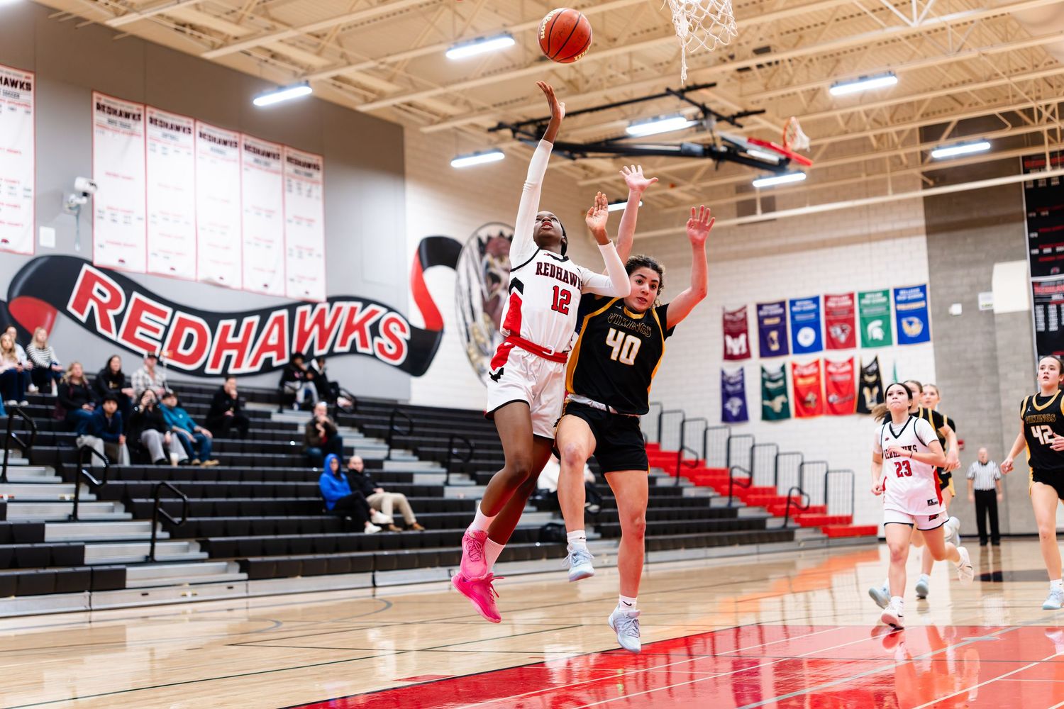 Basketball players compete for possession during an intense indoor game at a high school gymnasium.
