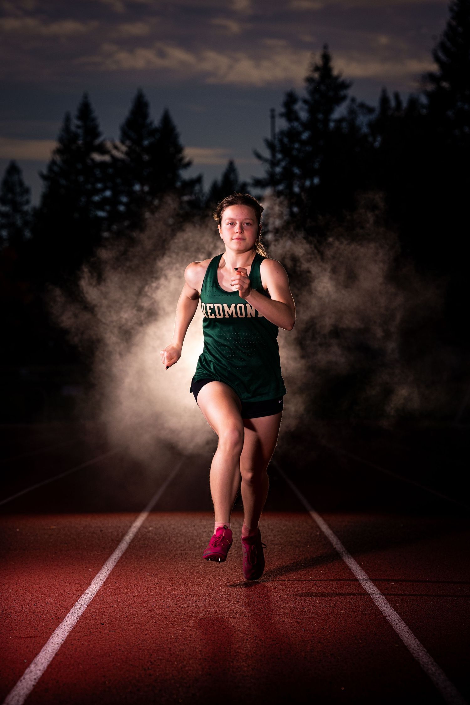 Dramatic sequence of an athlete in a green uniform starting from blocks on a red track at dusk with moody lighting.
