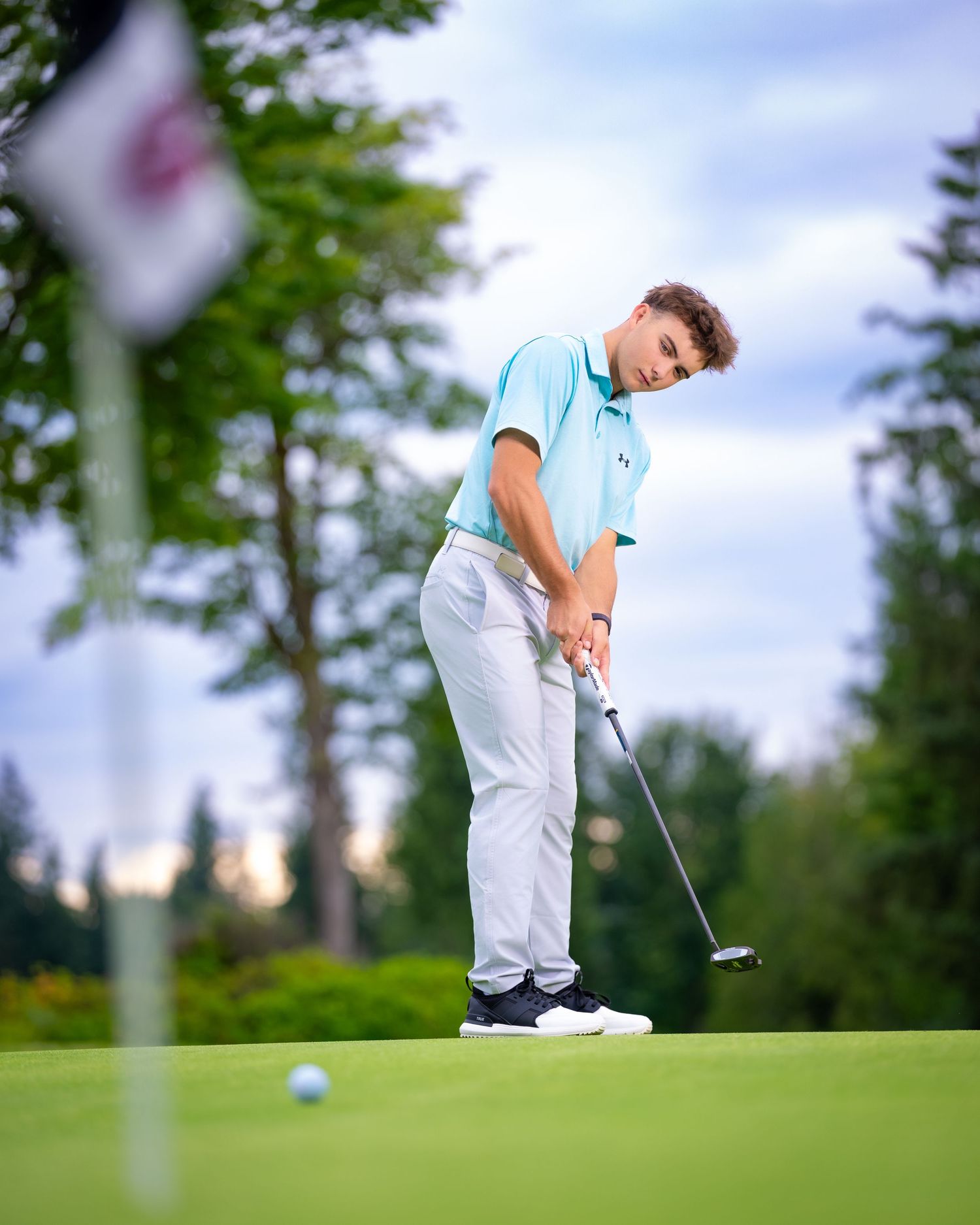 A golfer lines up a putt on a pristine green course with trees in the background.