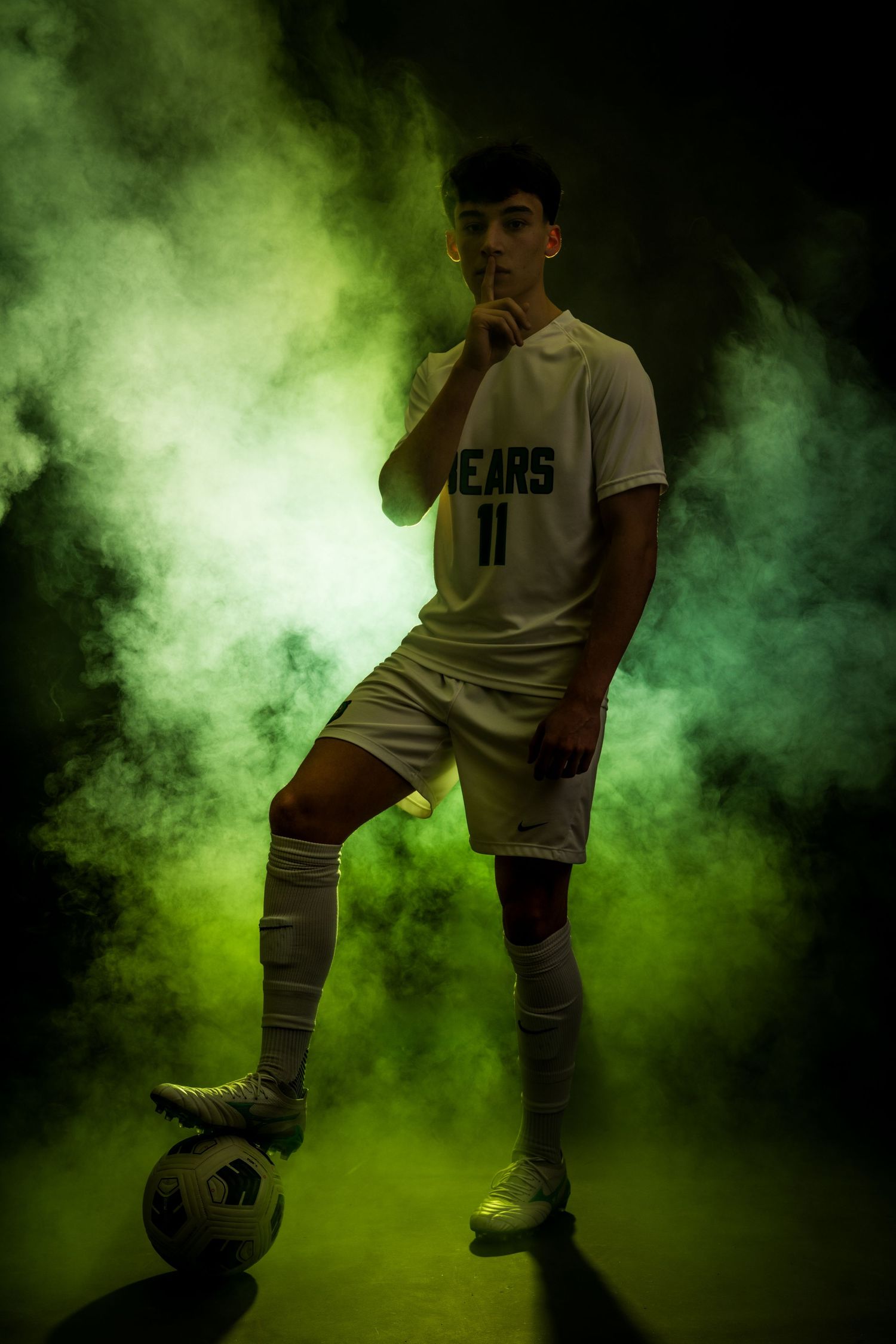 Soccer player silhouetted against green smoke performs tricks with ball in dramatic sequence of action shots.