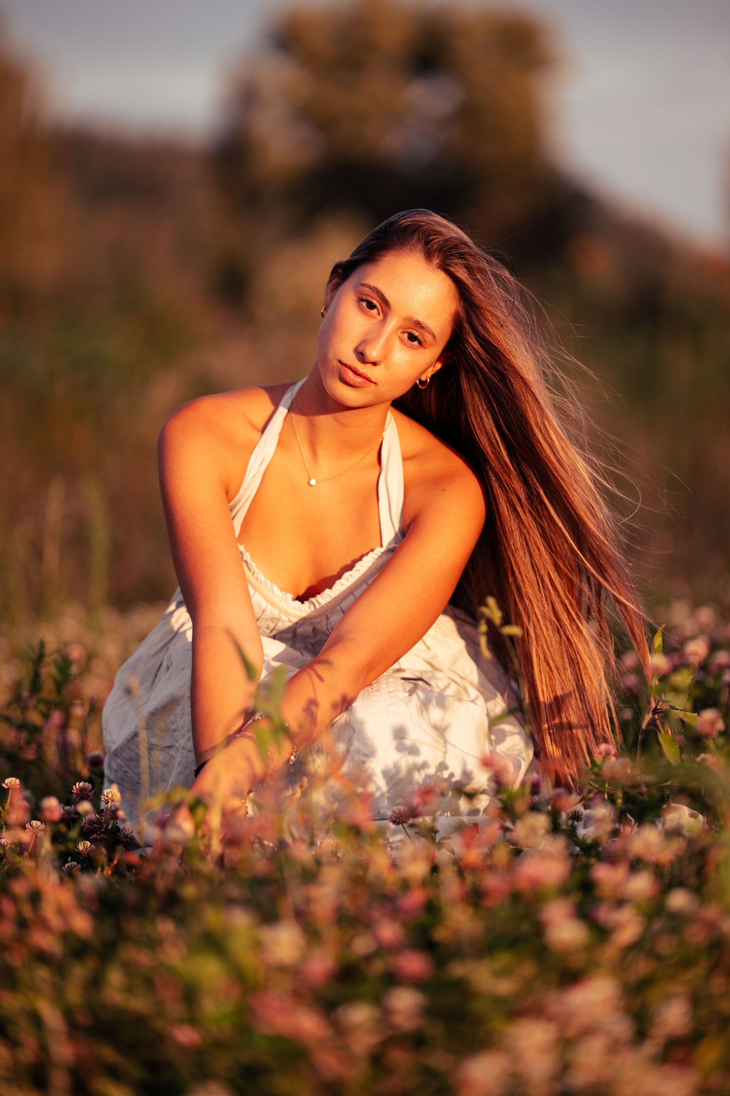 Person laying in a field of pink flowers during sunset wearing a white top.