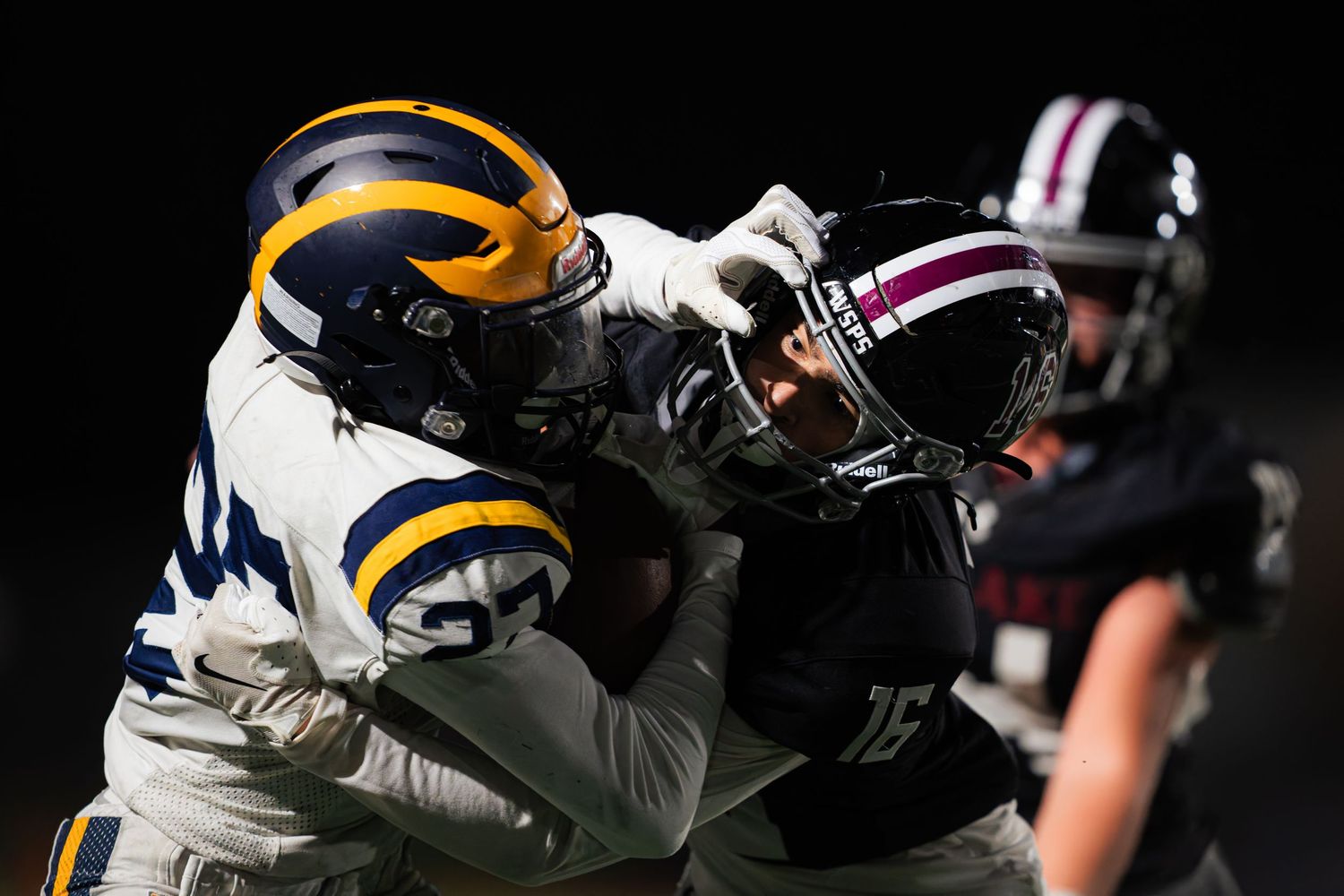 Football players in white and black uniforms clash during an intense game action moment on the field.