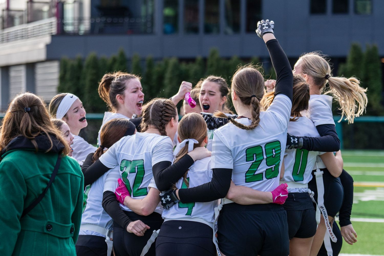A sports team celebrates together on a field wearing white jerseys with green accents and numbers.