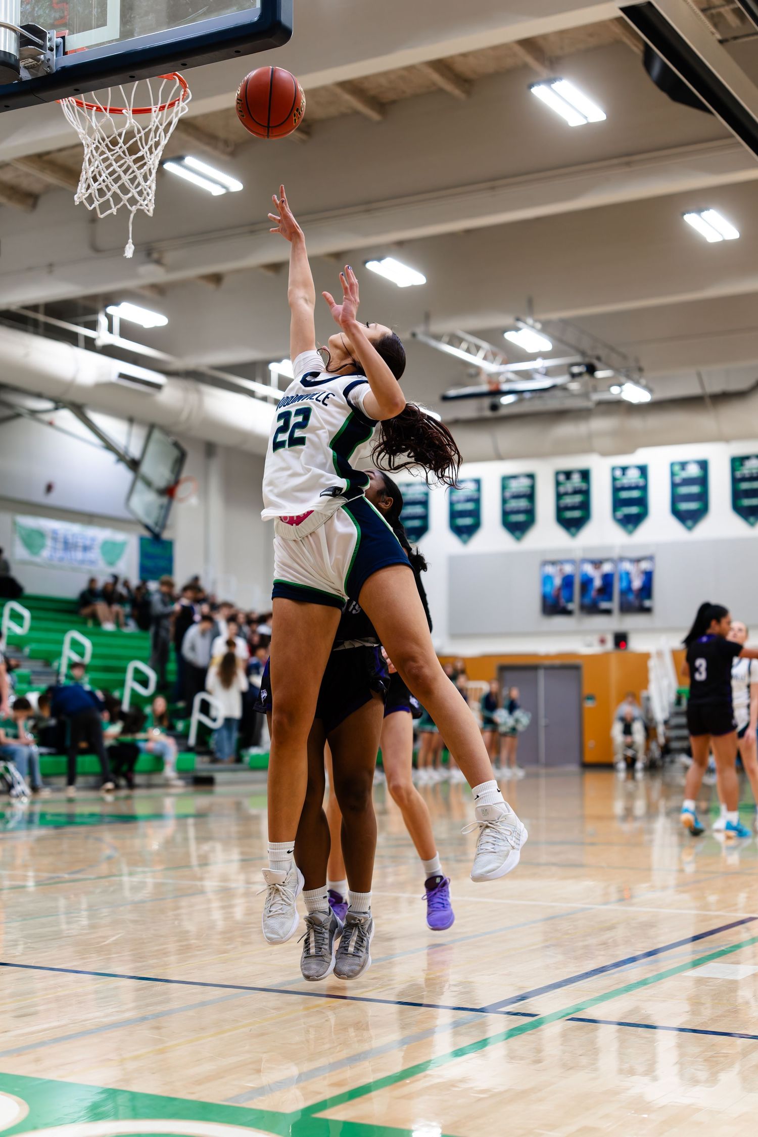 Basketball player jumps to make a layup shot during an indoor game on a polished gymnasium court.