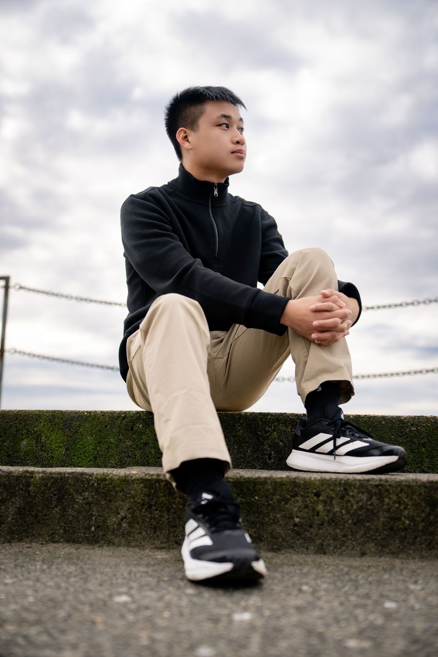 Person in casual attire sitting on concrete ledge wearing black and white sneakers.