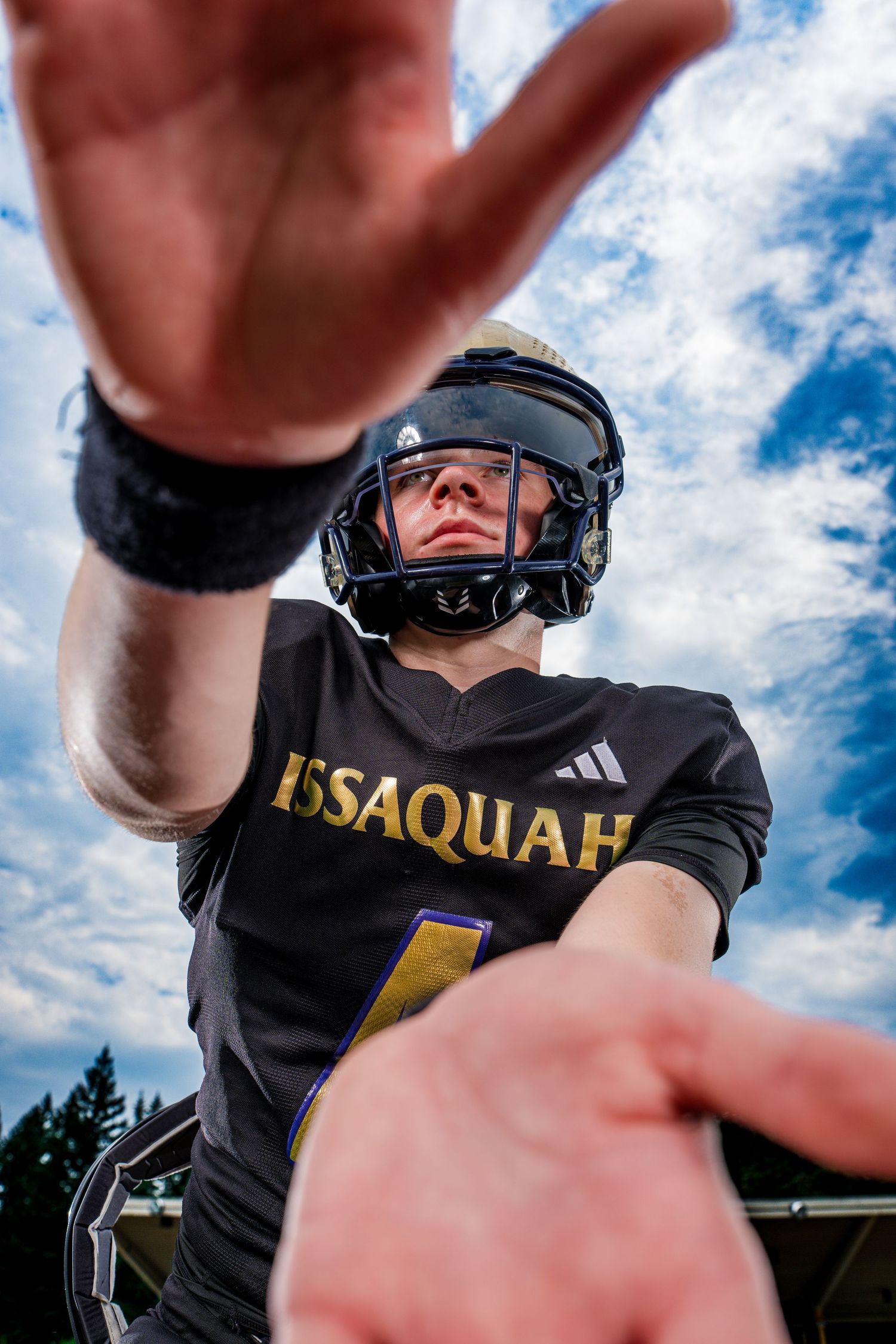 Football player in black Issaquah uniform and helmet photographed from below against blue sky.