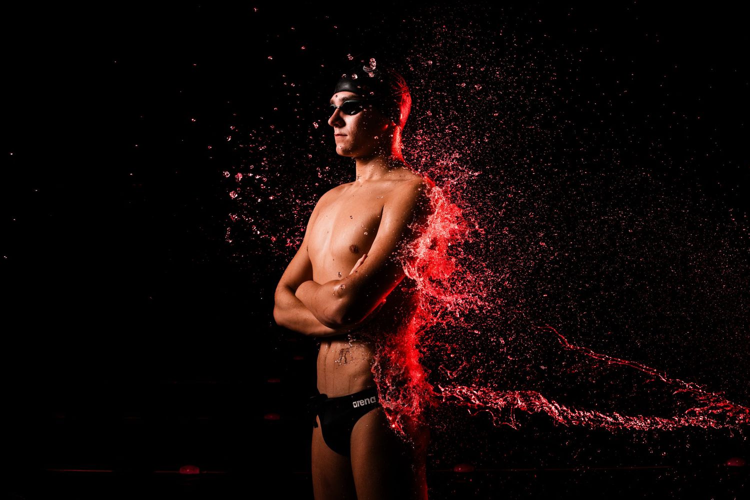 A dancer in silhouette poses against a dramatic red powder explosion effect in a dark studio setting.