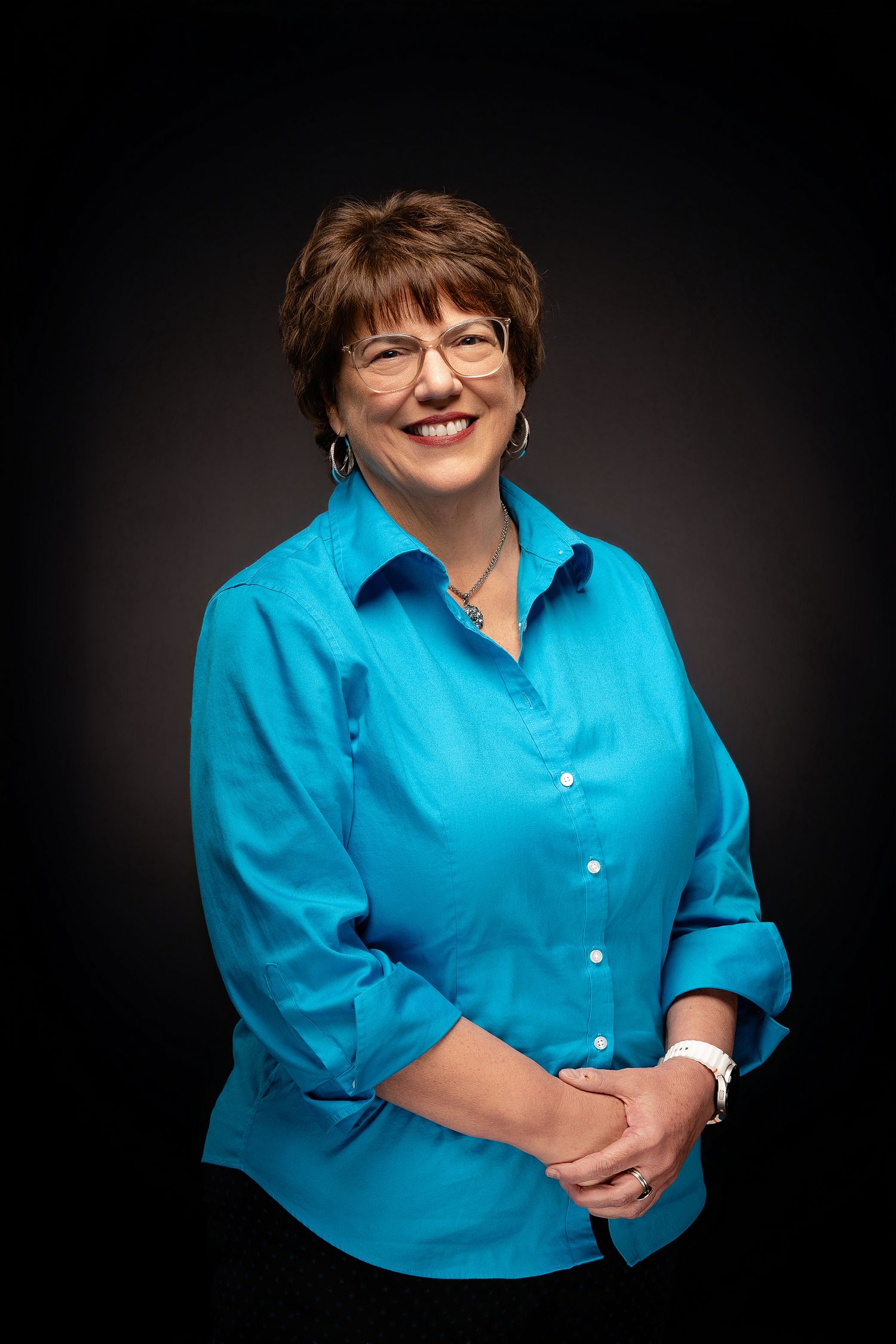 Professional portrait series showing person in bright turquoise blouse against dark background with warm smile and glasses.