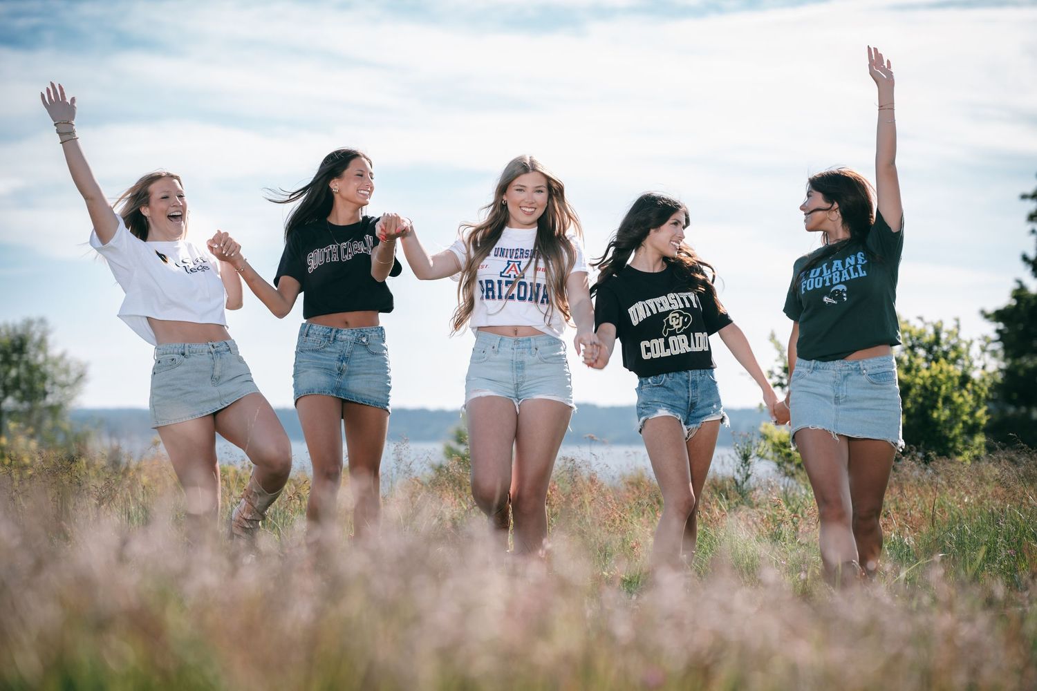 Group photo of friends posing playfully in a sunny meadow with mountains visible in the distance.
