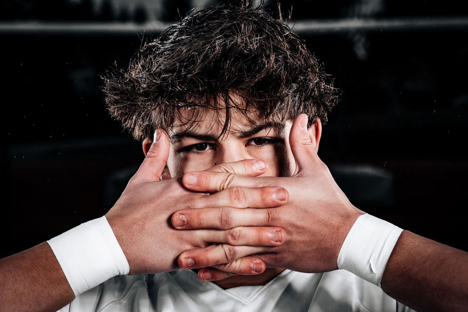 Person covering their face with both hands against dark background in dramatic black and white portrait.