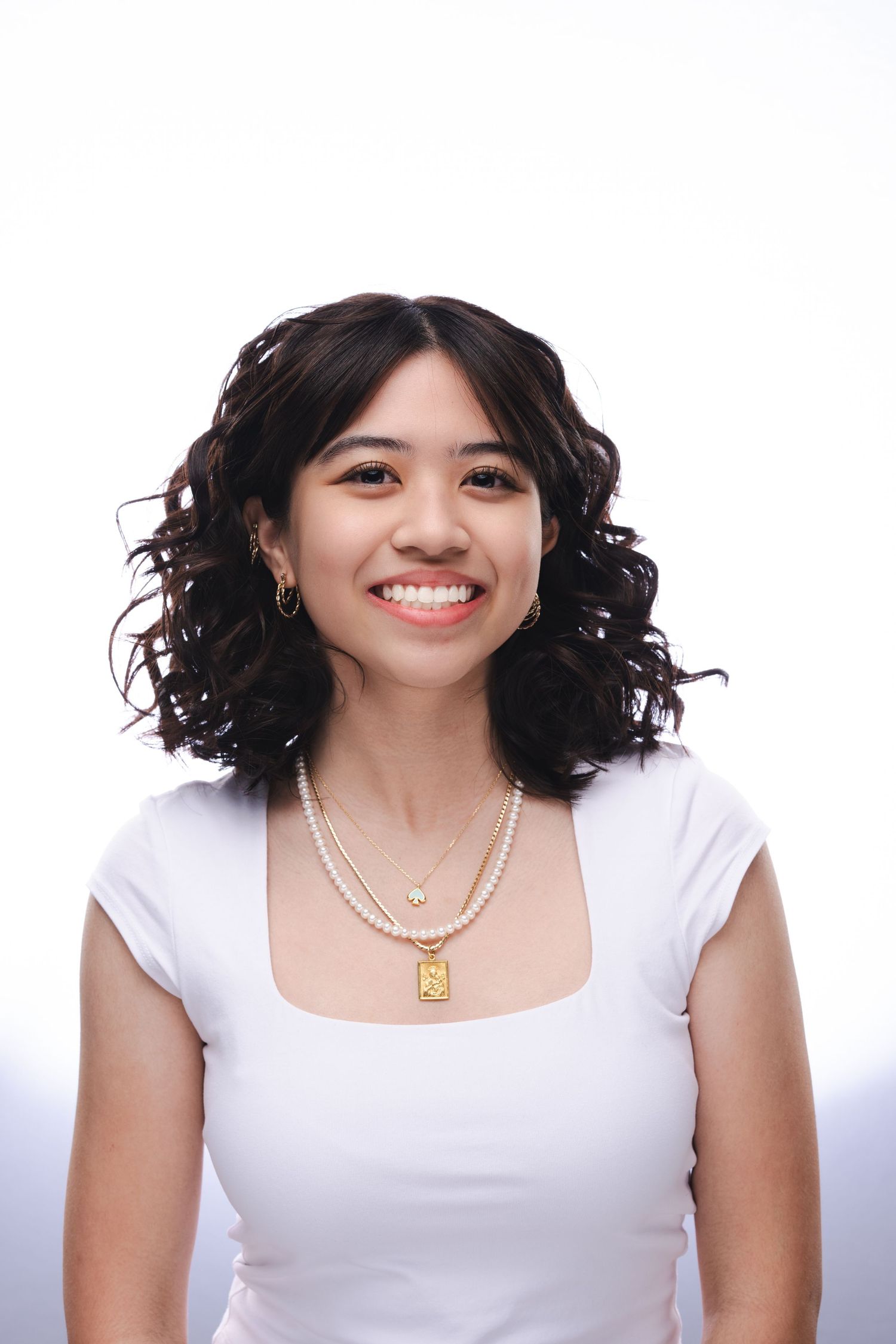 Three photos of a person with curly black hair wearing a white top and jewelry against a white background.