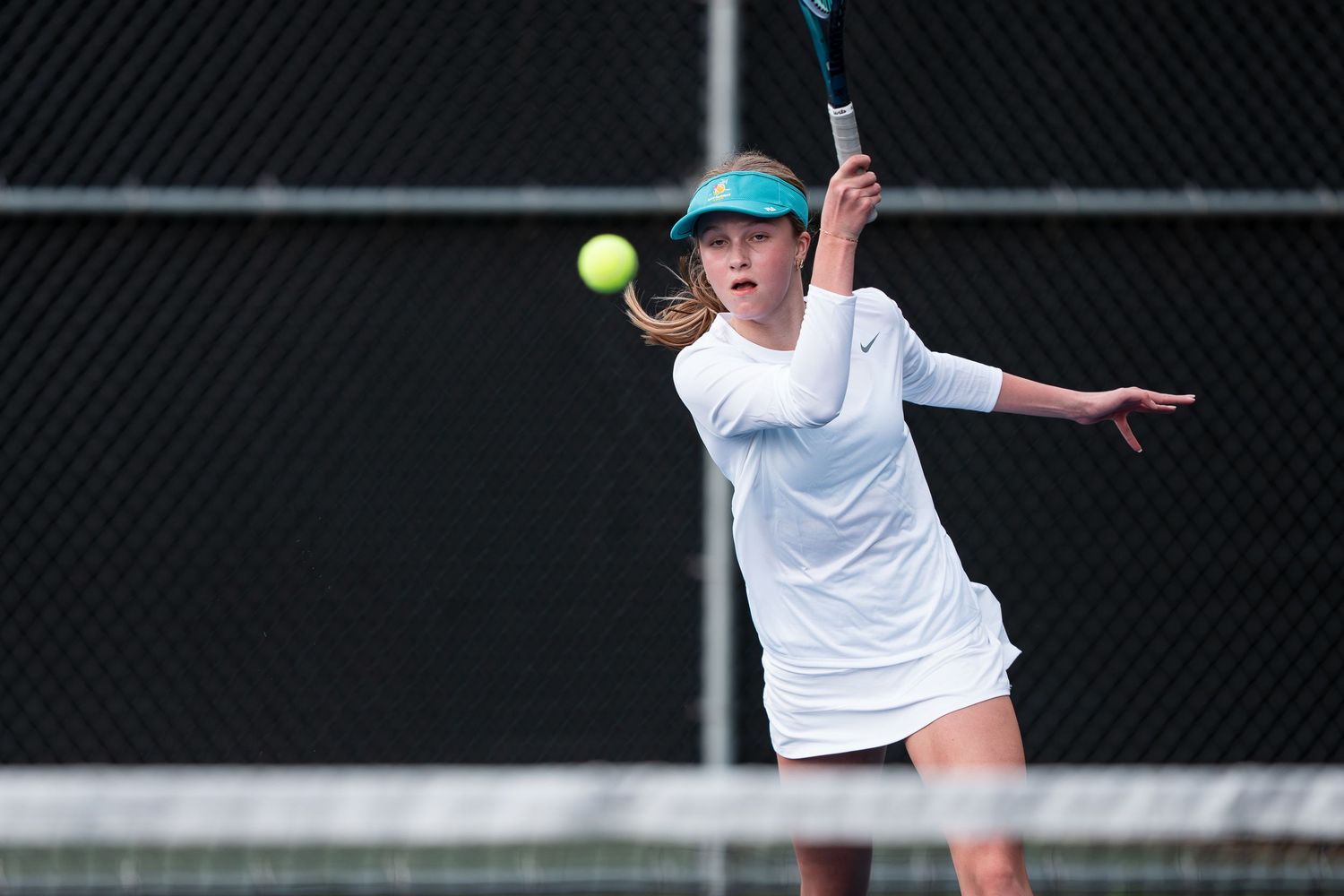 Tennis player wearing white shirt and shorts hits a forehand shot during a match on outdoor court.
