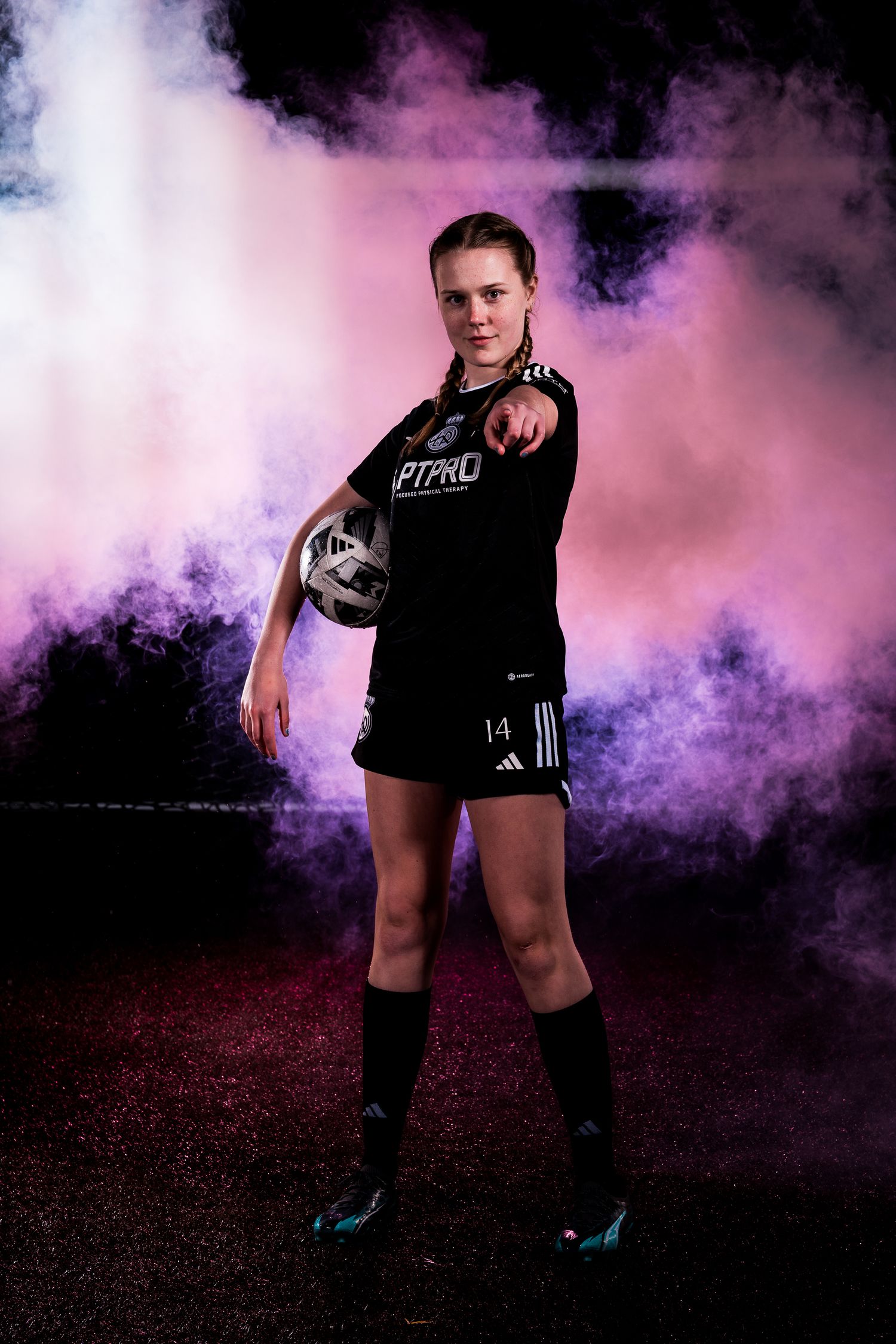 Athletic photoshoot featuring soccer gear and vibrant purple smoke effects against dark background.