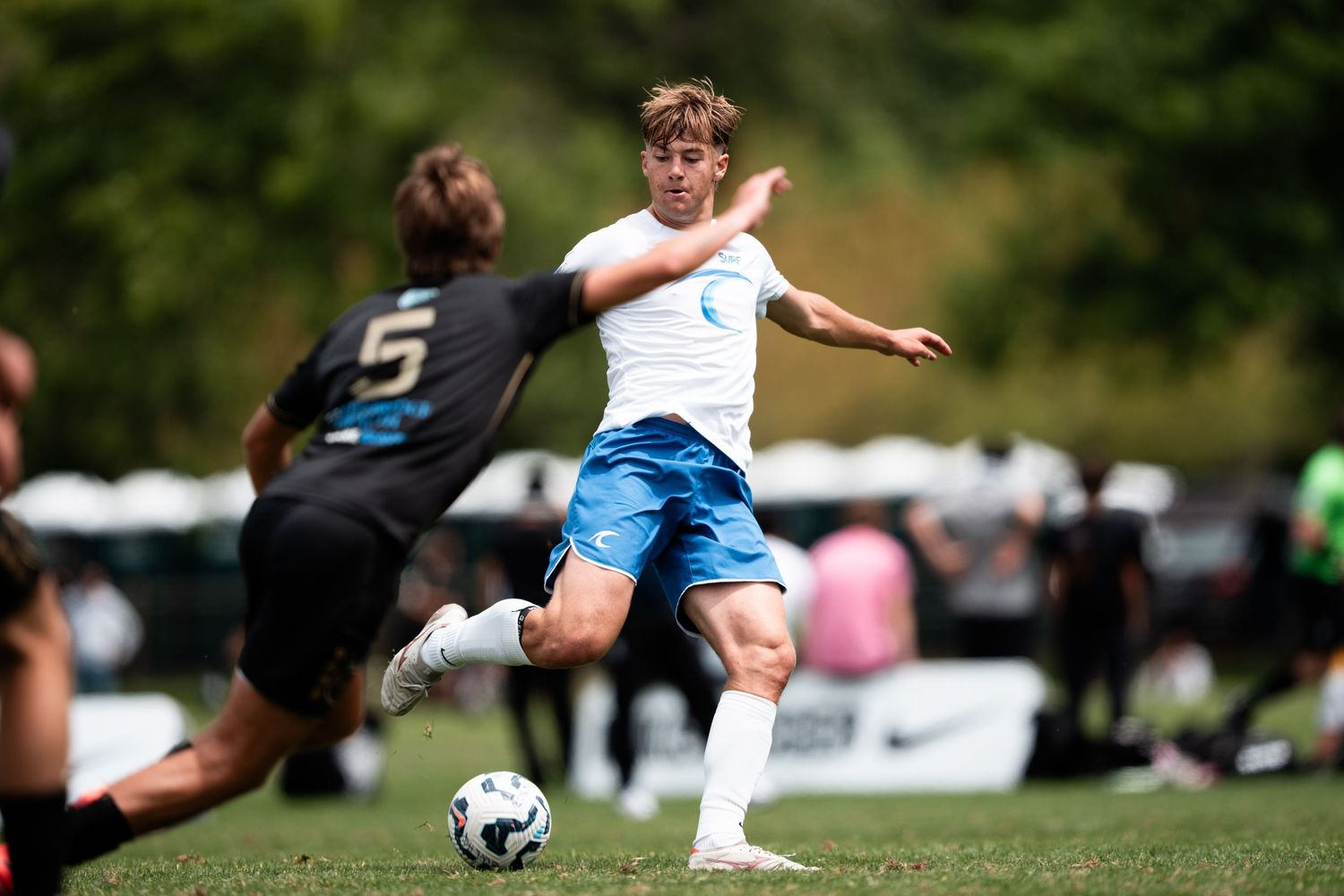 Soccer players in blue and white uniforms compete for ball control during an intense match on grass field.