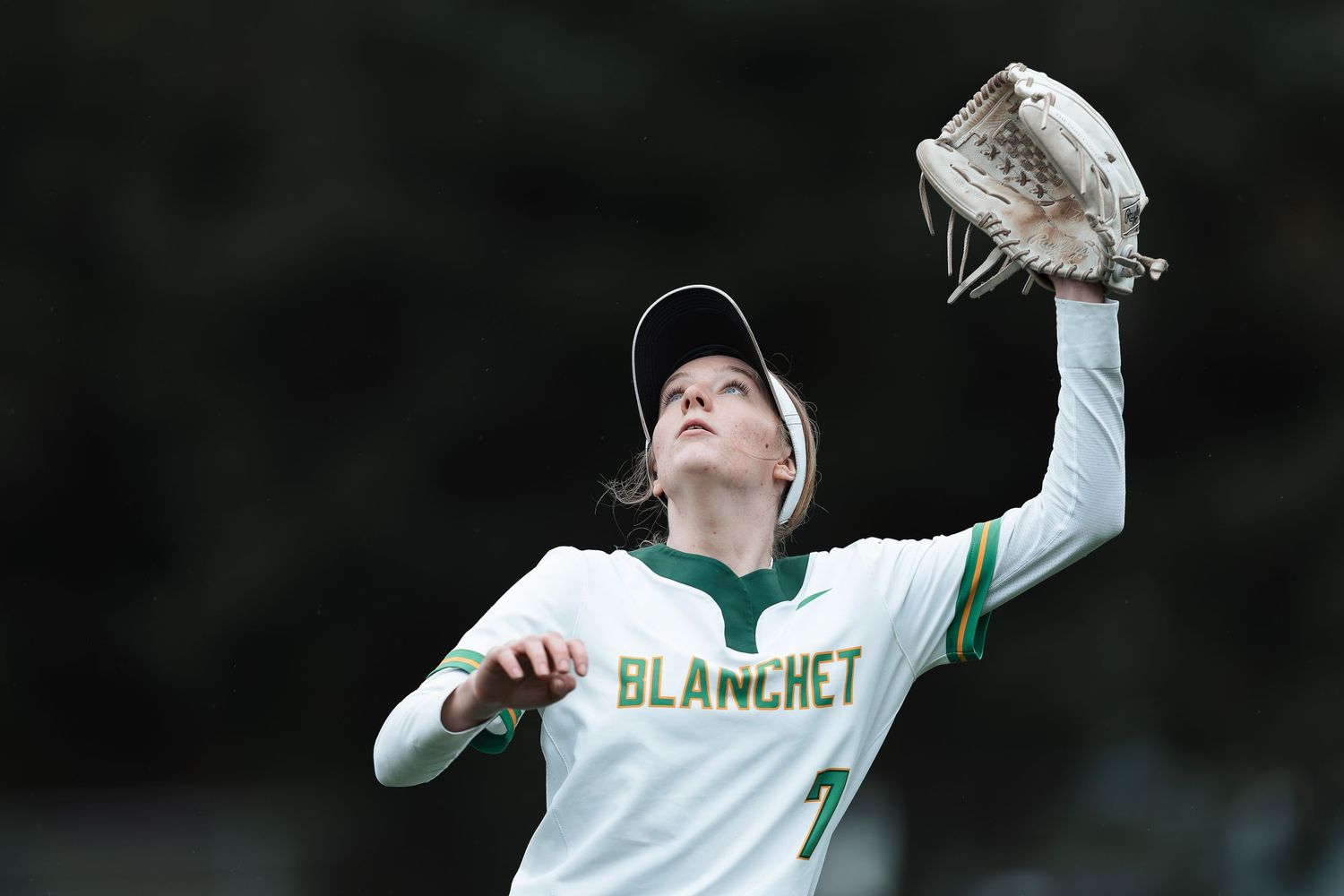 Baseball player in white uniform makes a leaping catch against a dark background during a game.