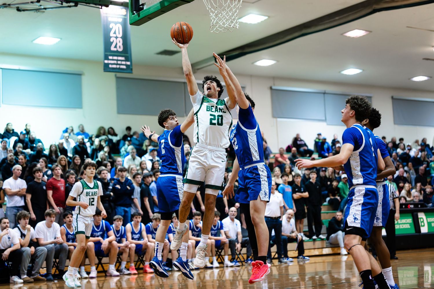Basketball player takes a jump shot during an intense game while defenders try to block the attempt.