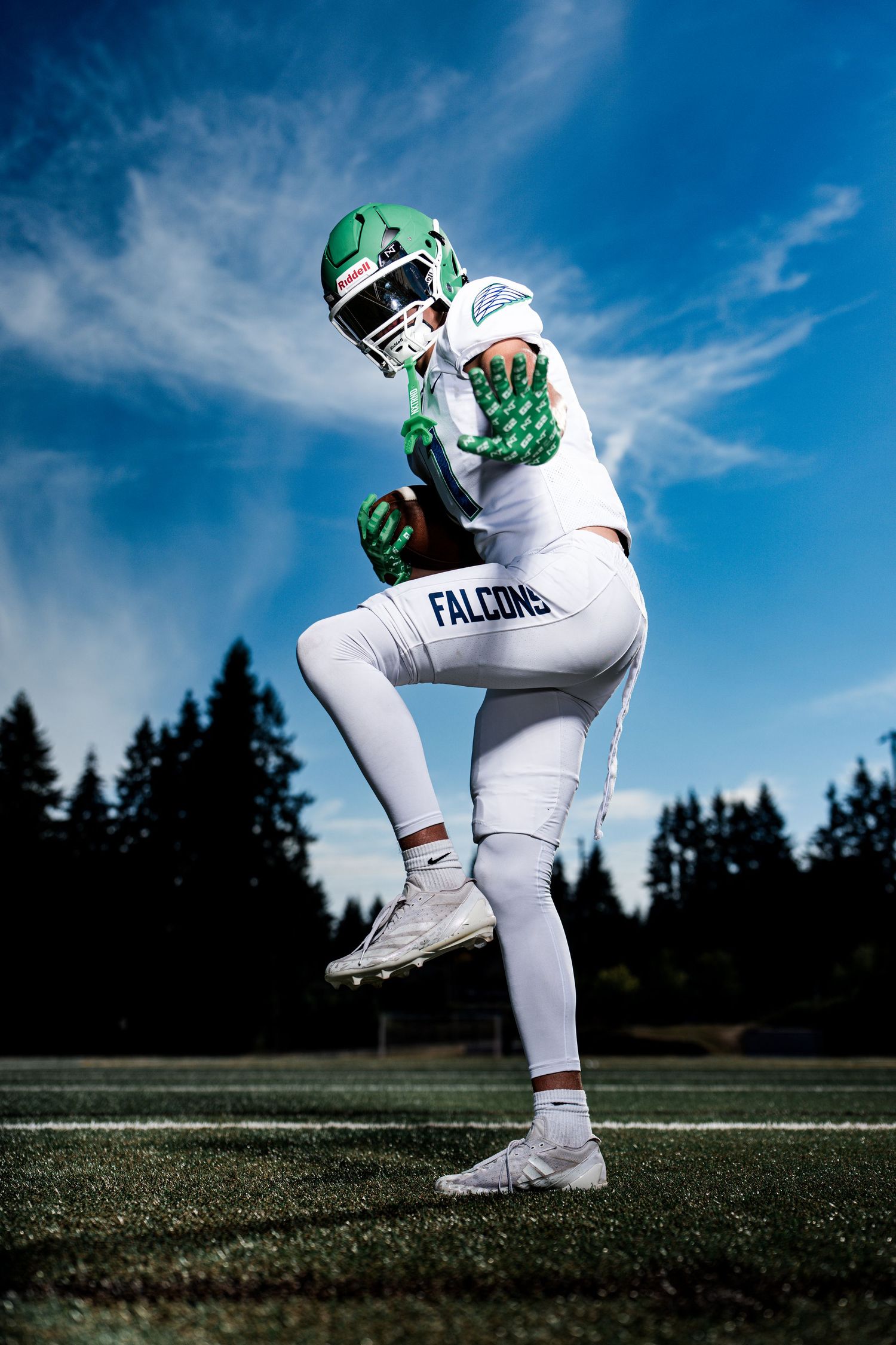 Football player in white uniform and green helmet crouches on field during practice.