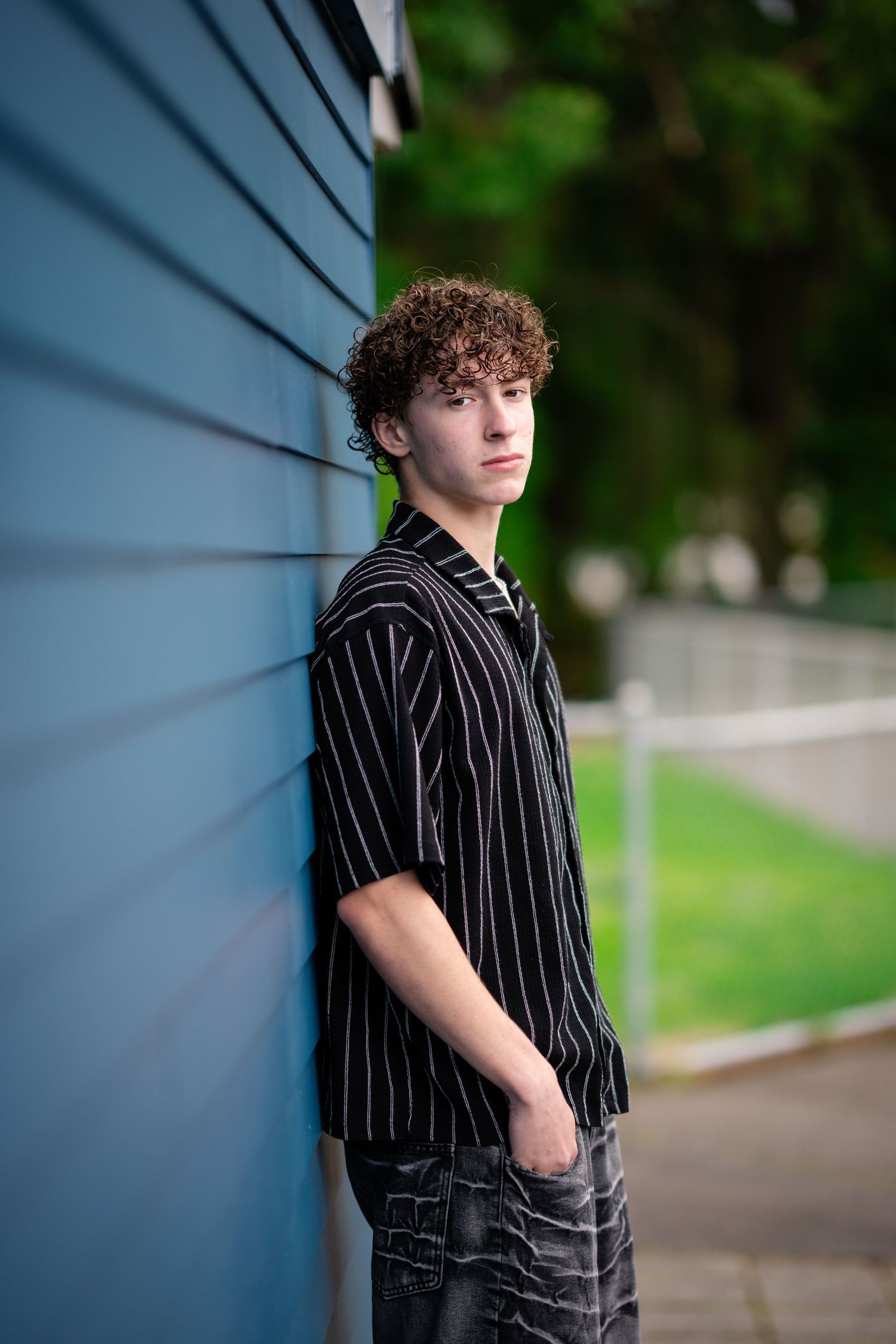 Person in pinstriped shirt leans against blue wall in casual outdoor portrait.