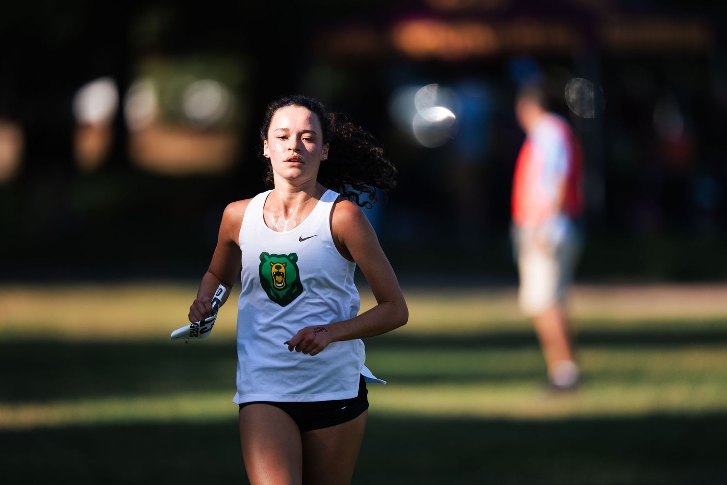 Athletes compete in a cross country running race on a sunny day across grassy terrain.