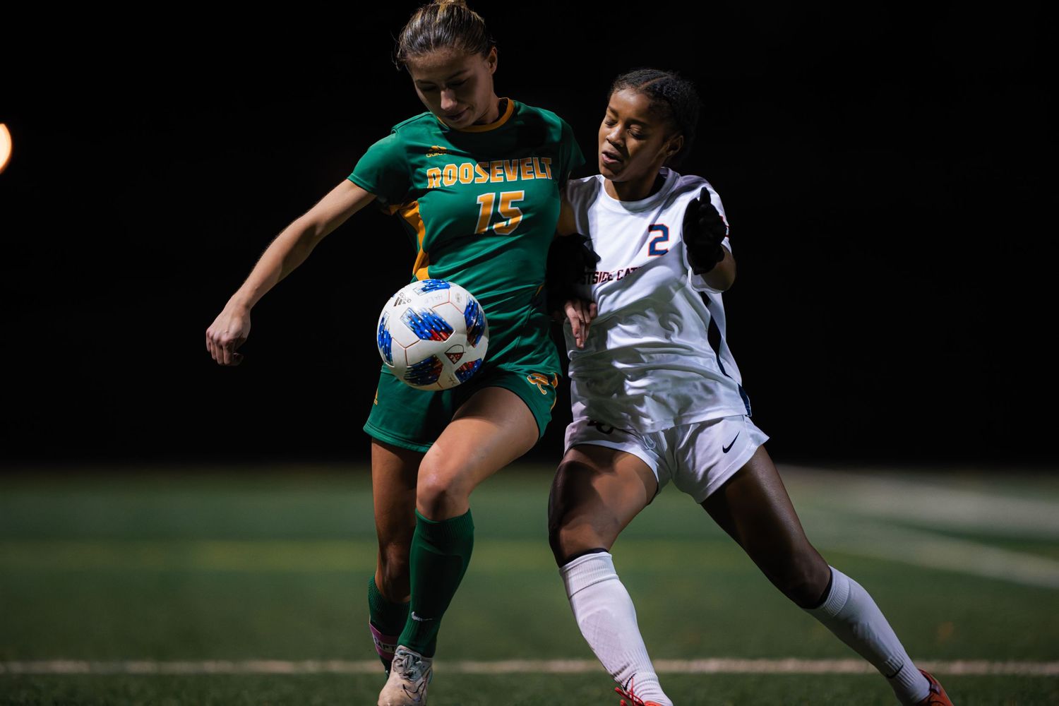 Two soccer players compete for possession of the ball during an intense match on a night field.