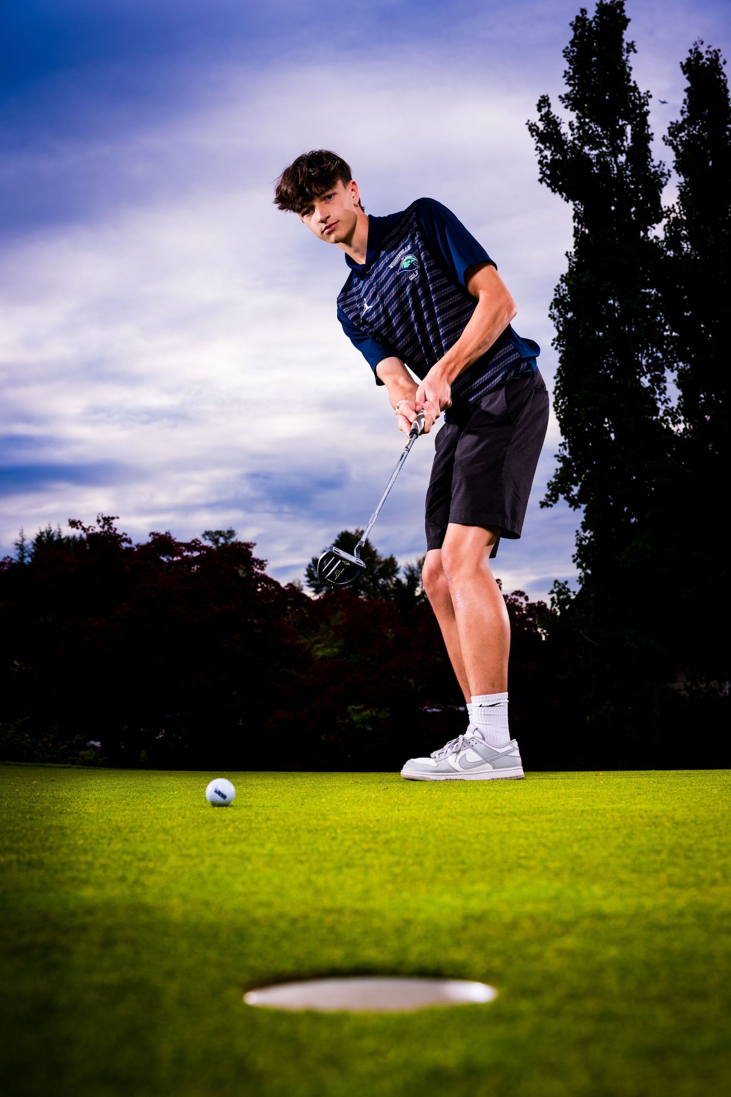 Golfer in navy polo prepares to putt on green during sunset.