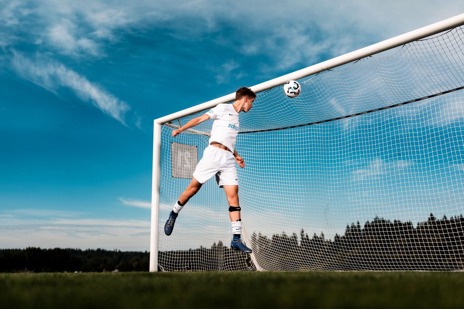 Soccer goalkeeper making a diving save against blue sky background.