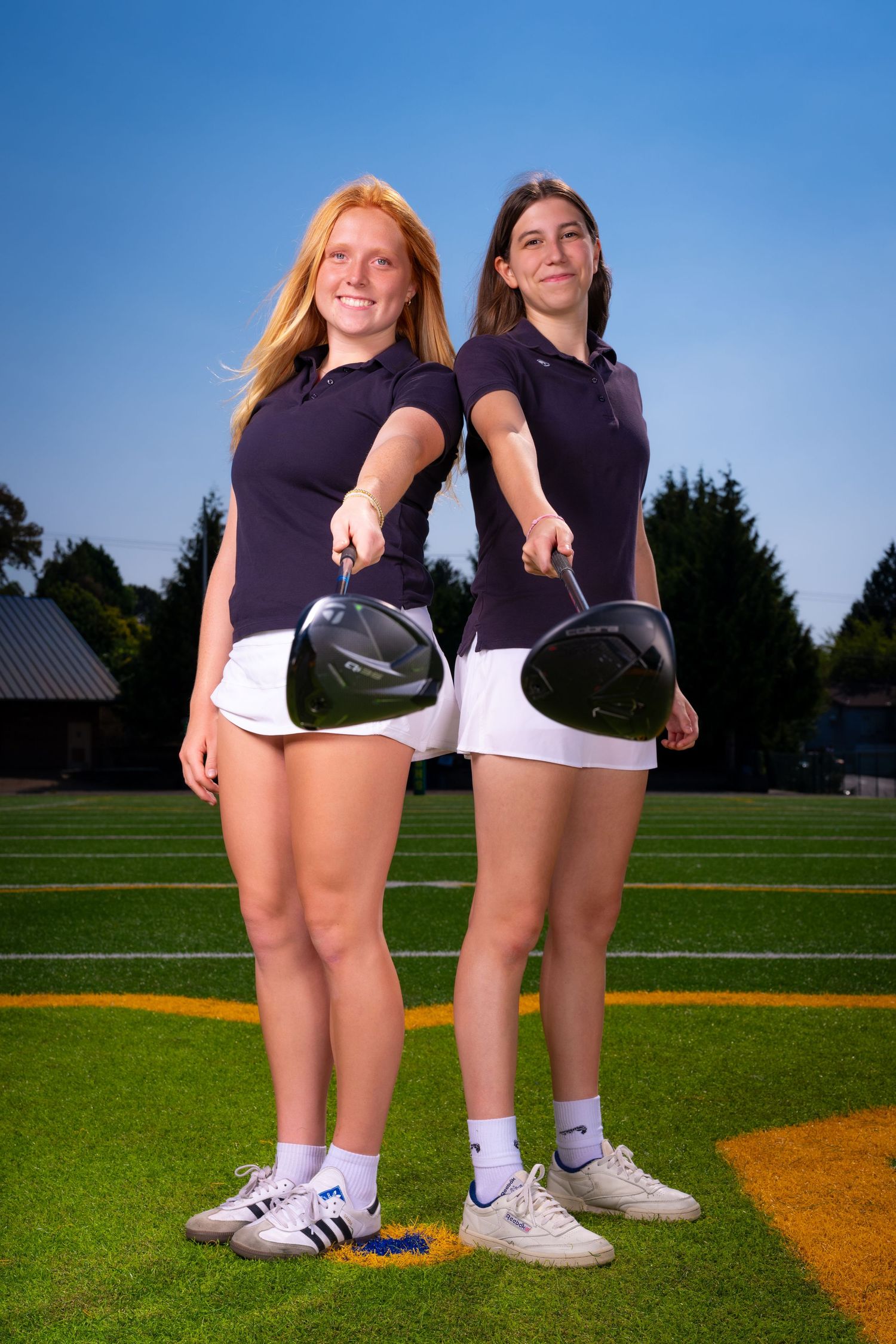 Two athletes in dark uniforms pose together on a sports field.