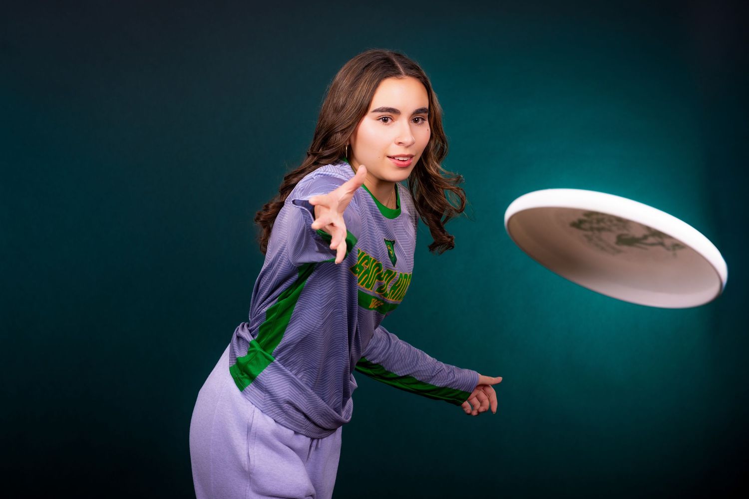 Ultimate frisbee player in purple outfit throwing disc against dark background.