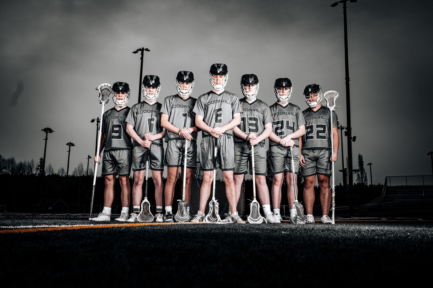Baseball team members sit together on a bench in dramatic black and white lighting during a game.