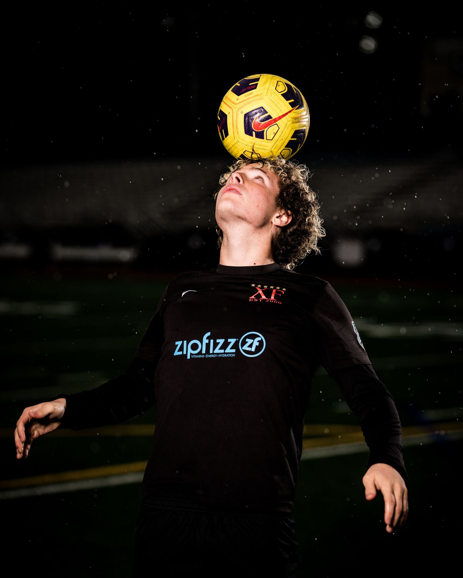 Soccer player in black jersey practices ball control drills at night on outdoor field.