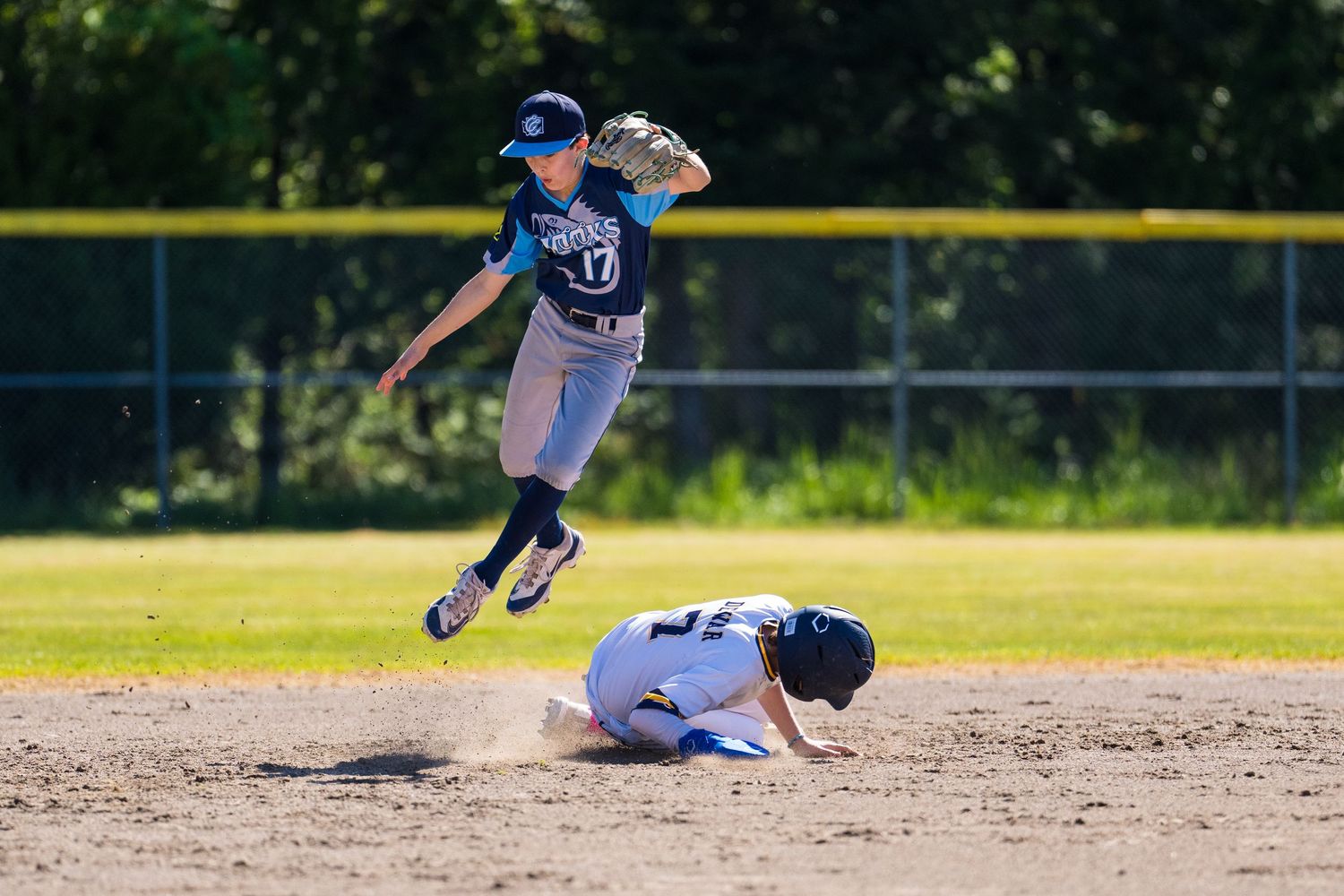 Baseball player sliding into base during intense game action as defender attempts to make the tag.