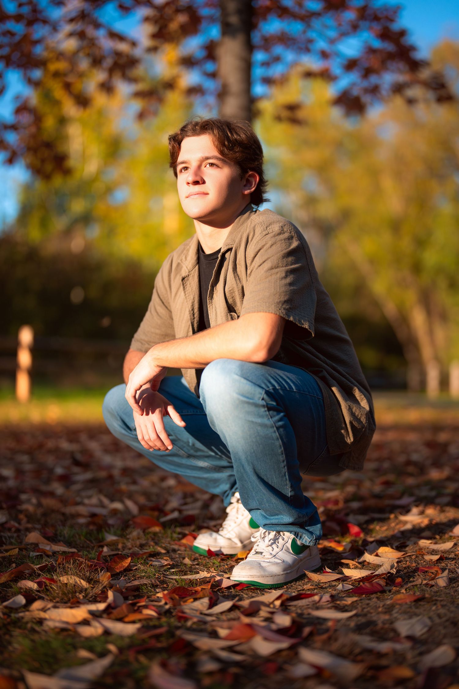 Person sitting among fallen autumn leaves in golden sunlight.