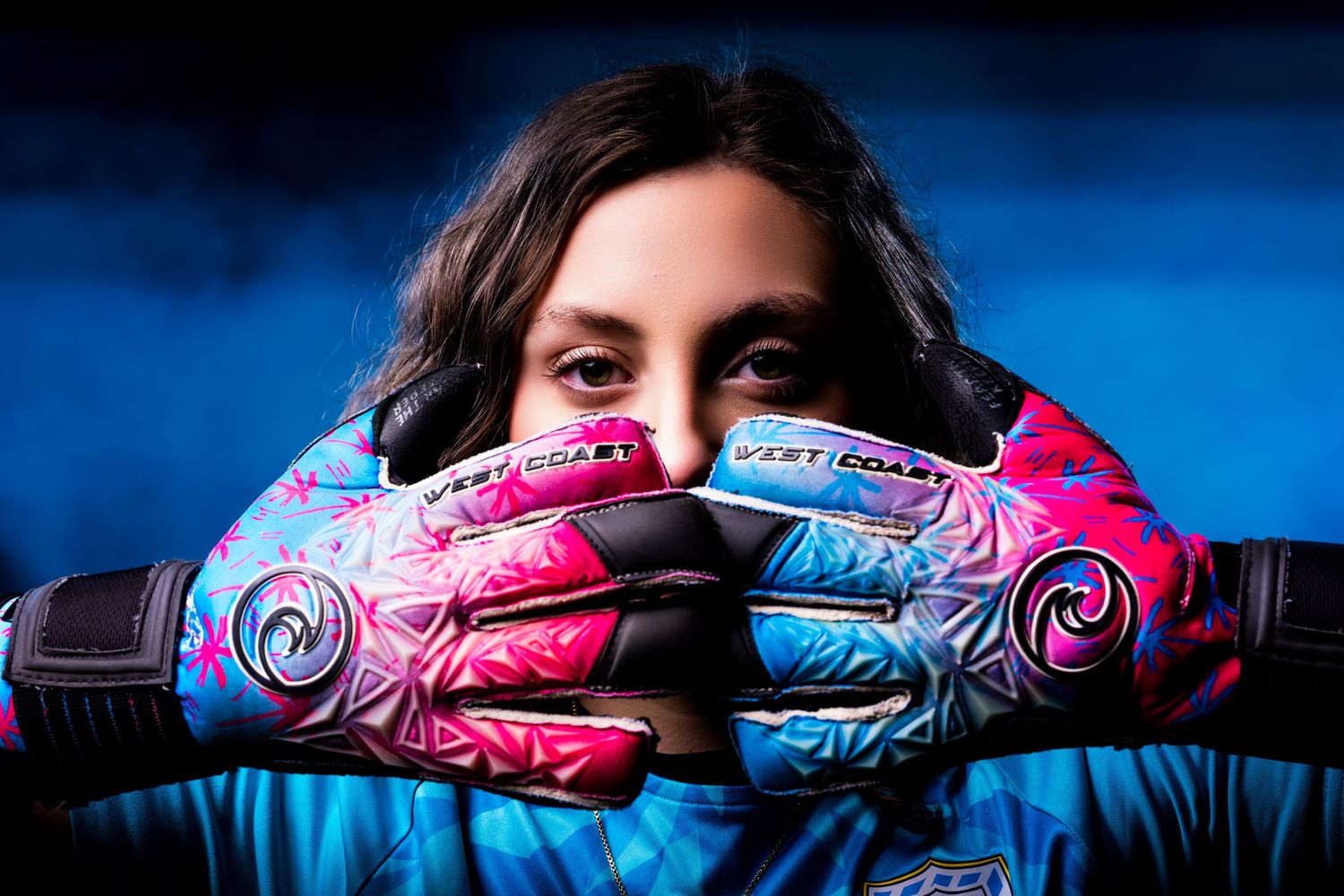 Pink and blue soccer cleats with swirling designs photographed against a dark blue background.