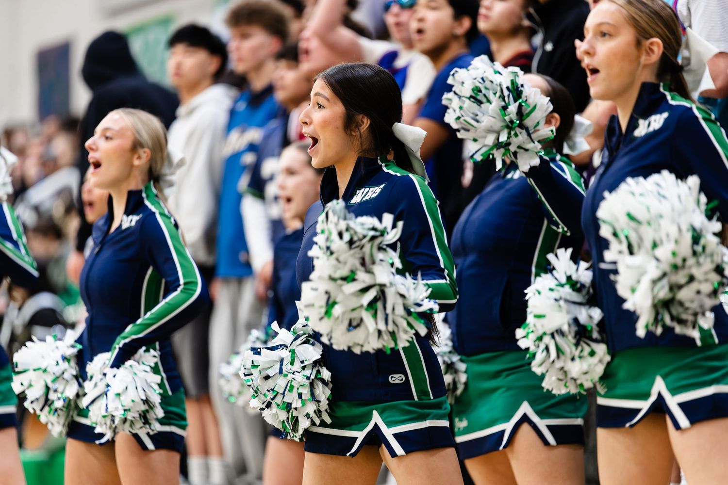 Cheerleaders in green and white uniforms perform in formation during a sporting event.