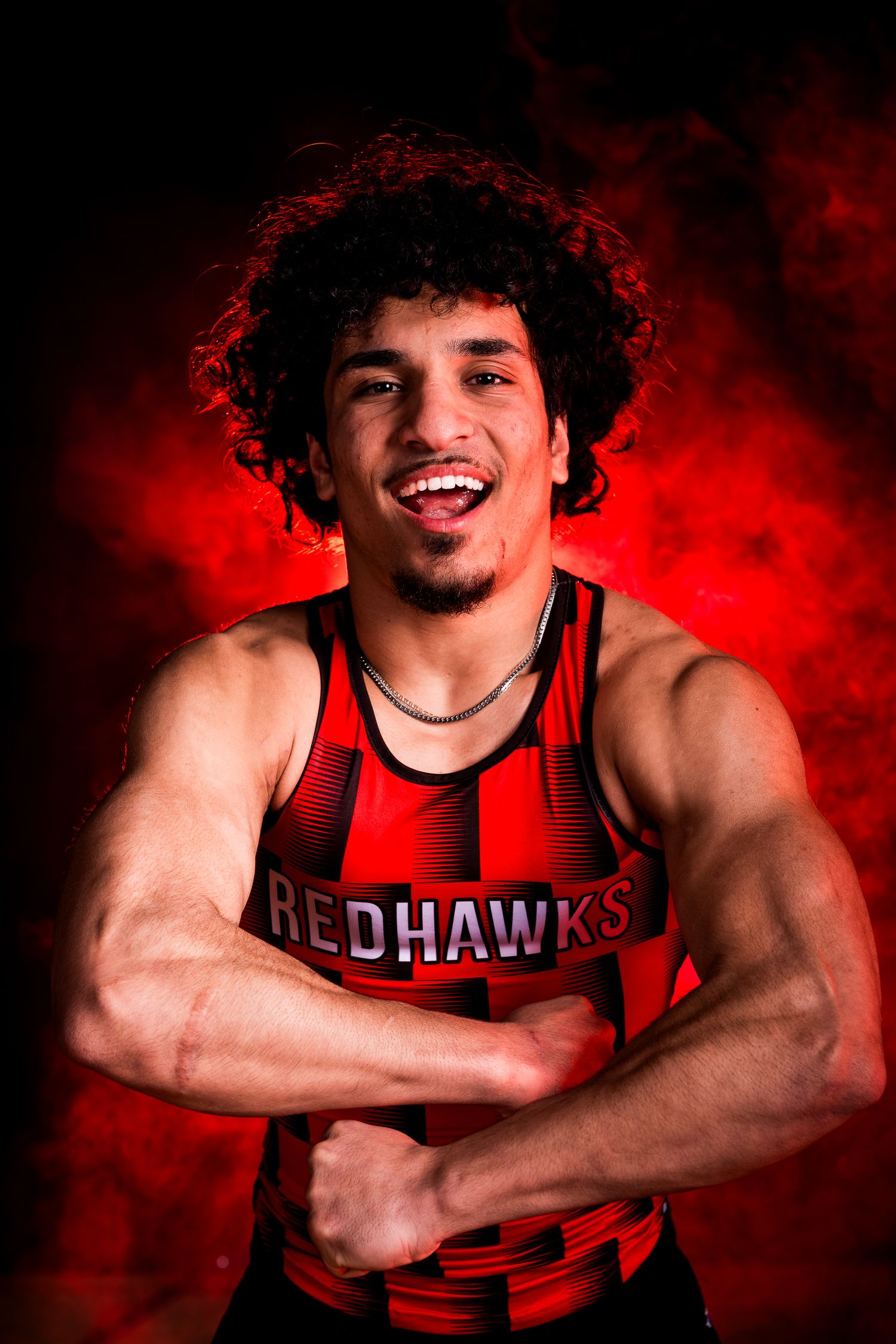 RedHawks athlete in red jersey poses against dramatic red smoke background.
