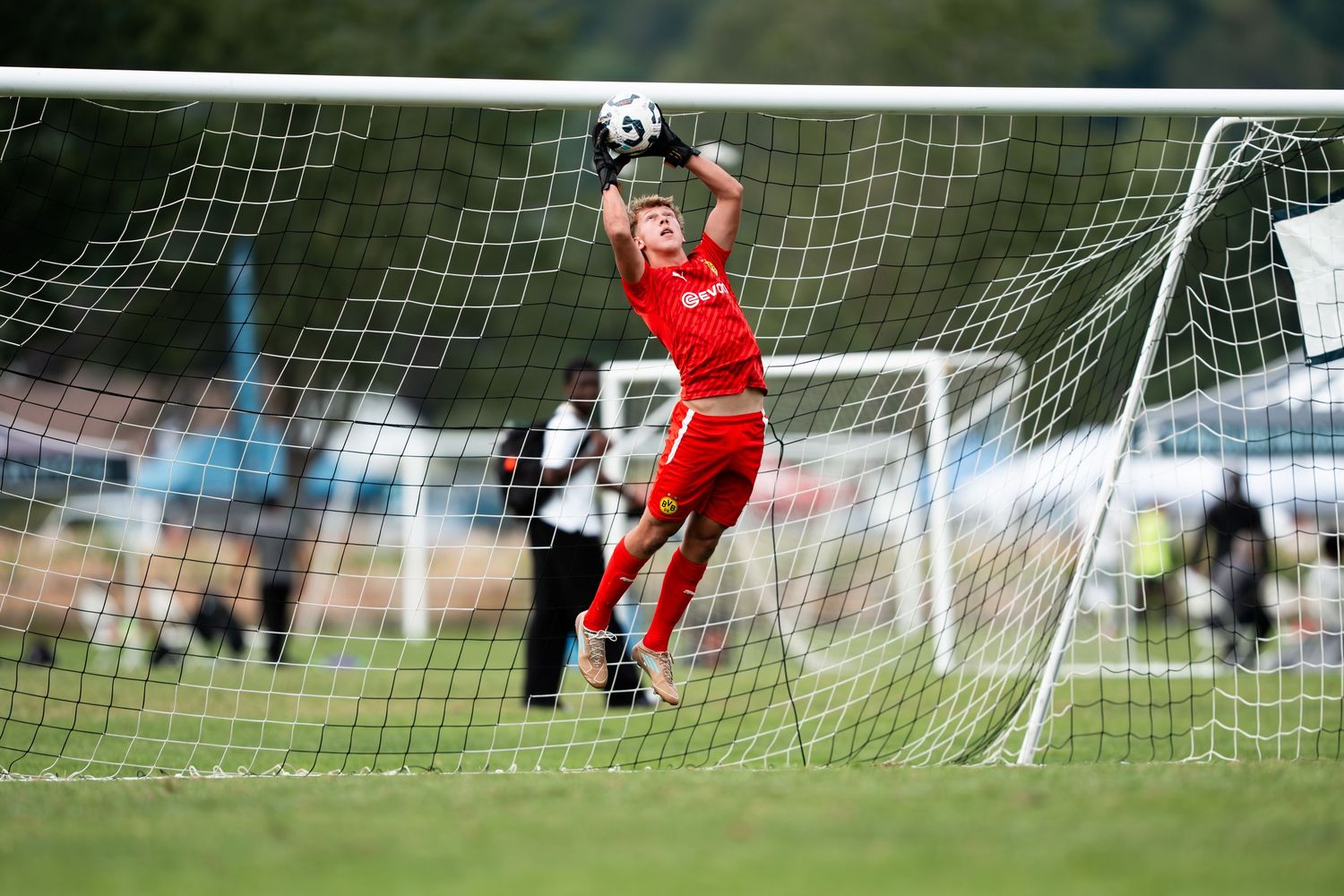 Soccer goalie in red uniform leaping to make a diving save during a match.