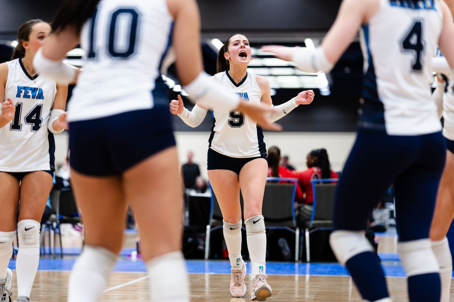 Volleyball players communicate during an indoor match with teammates visible on court.