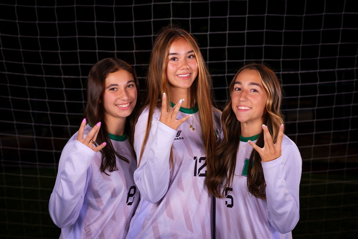 Soccer teammates in matching lavender sweatshirts pose together in front of a goal net at night.