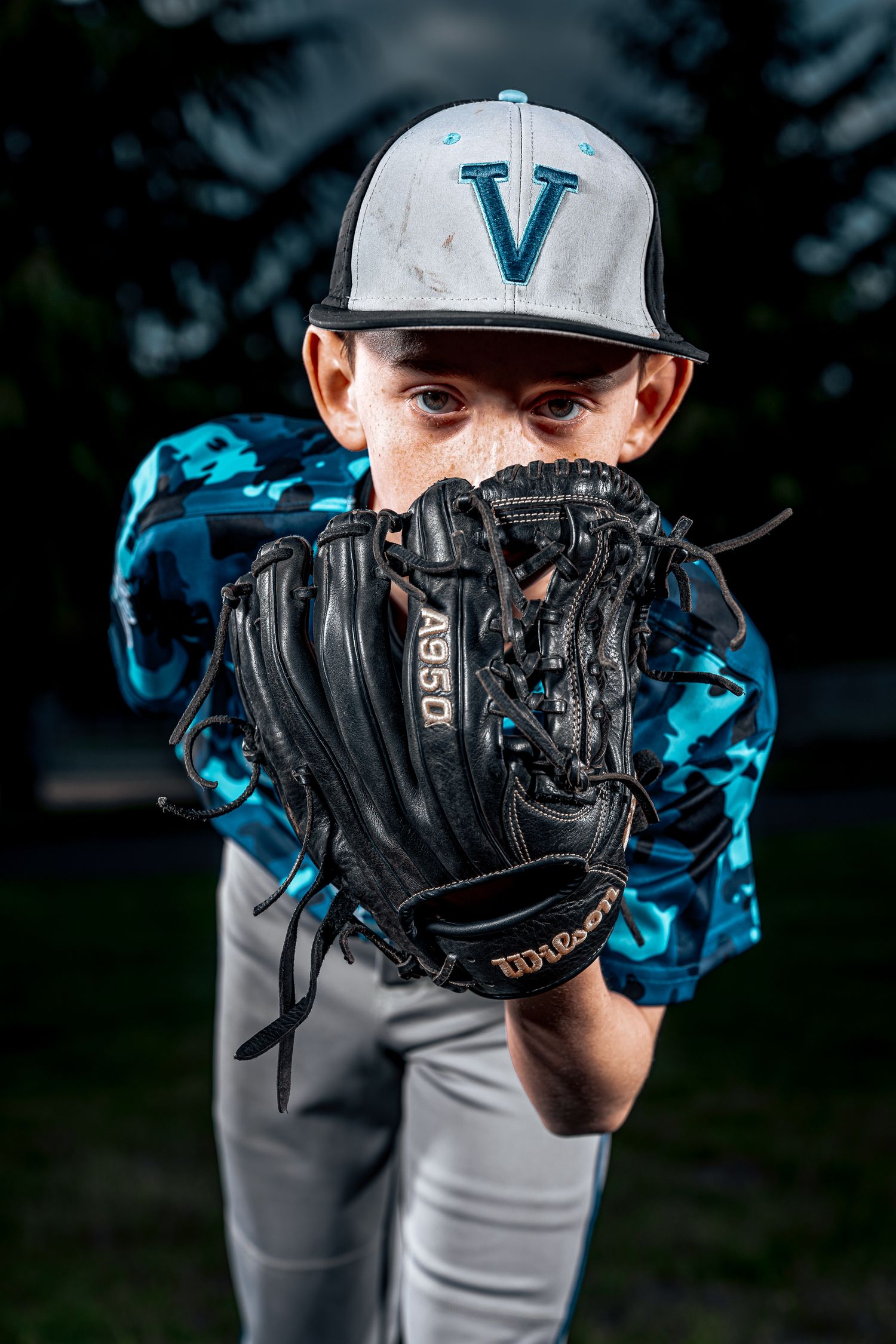 Close-up of baseball glove with teal team logo cap in background.