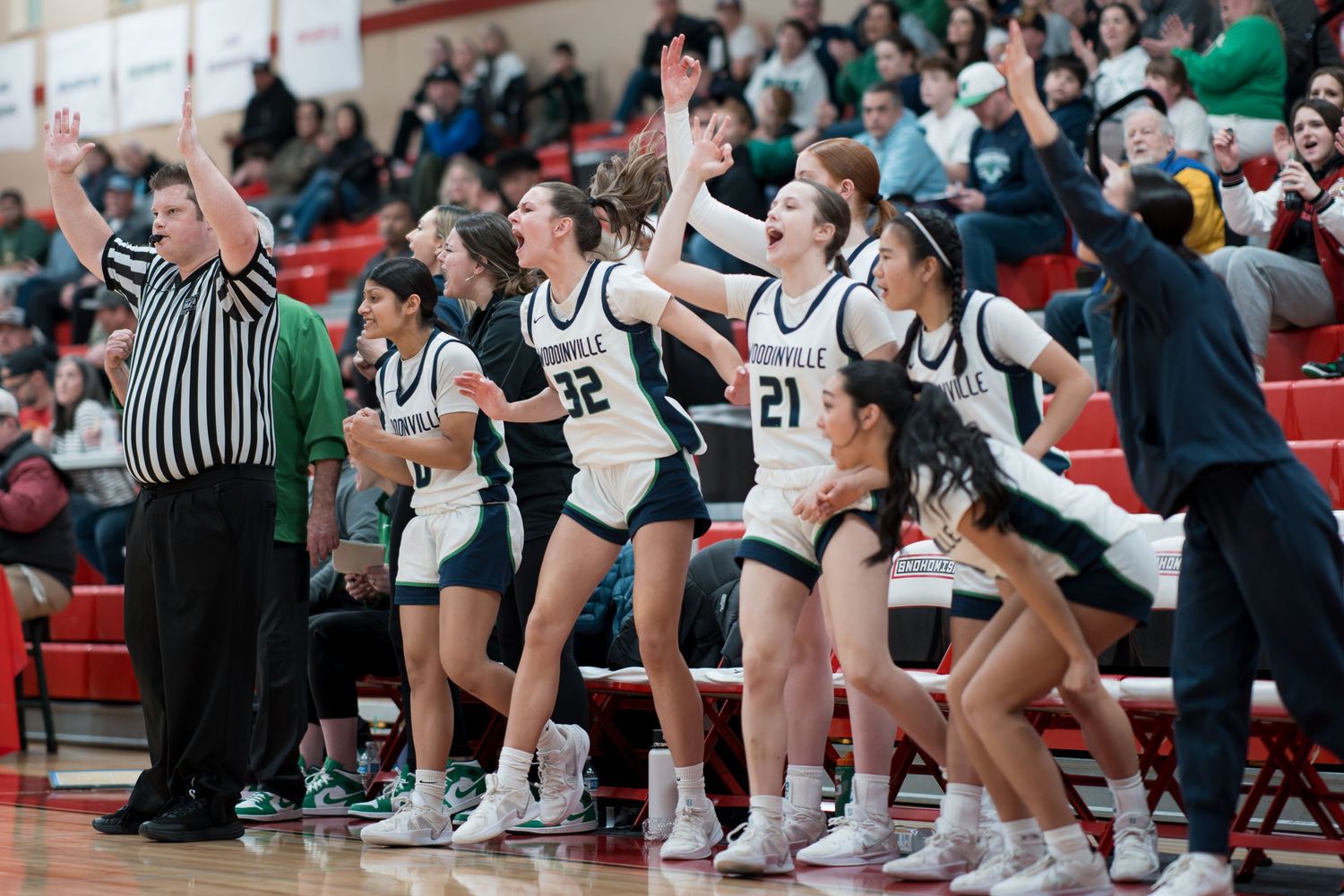 Basketball players and coaches sit on the sideline bench during an intense game at a high school gymnasium.