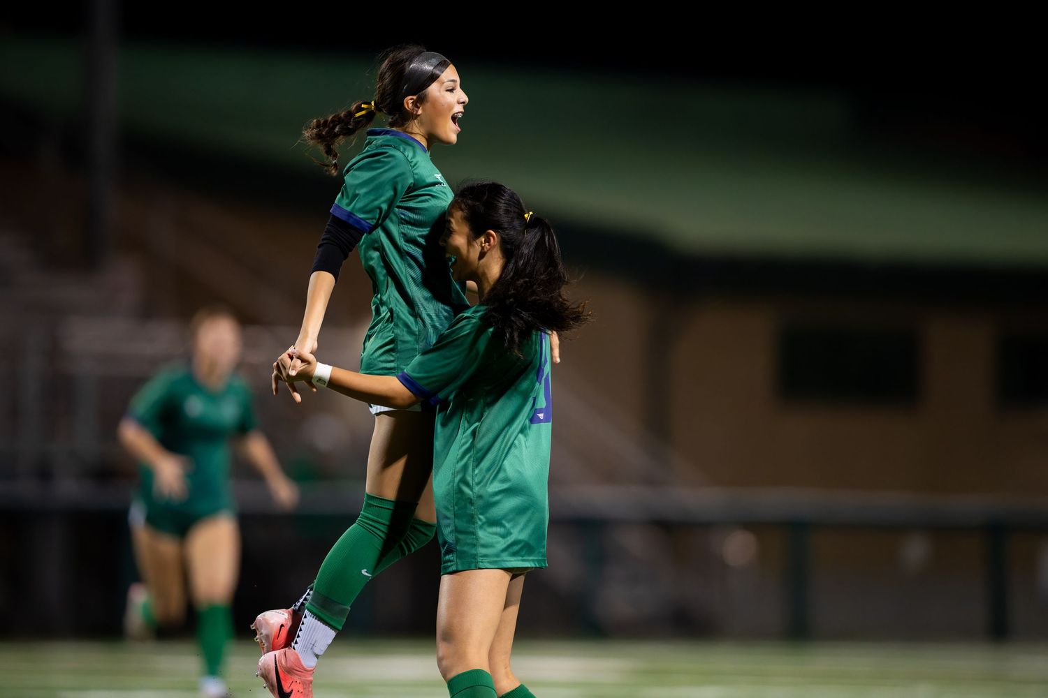 Soccer players in green jerseys celebrate a goal during a match with energetic jumping and hugging motions.