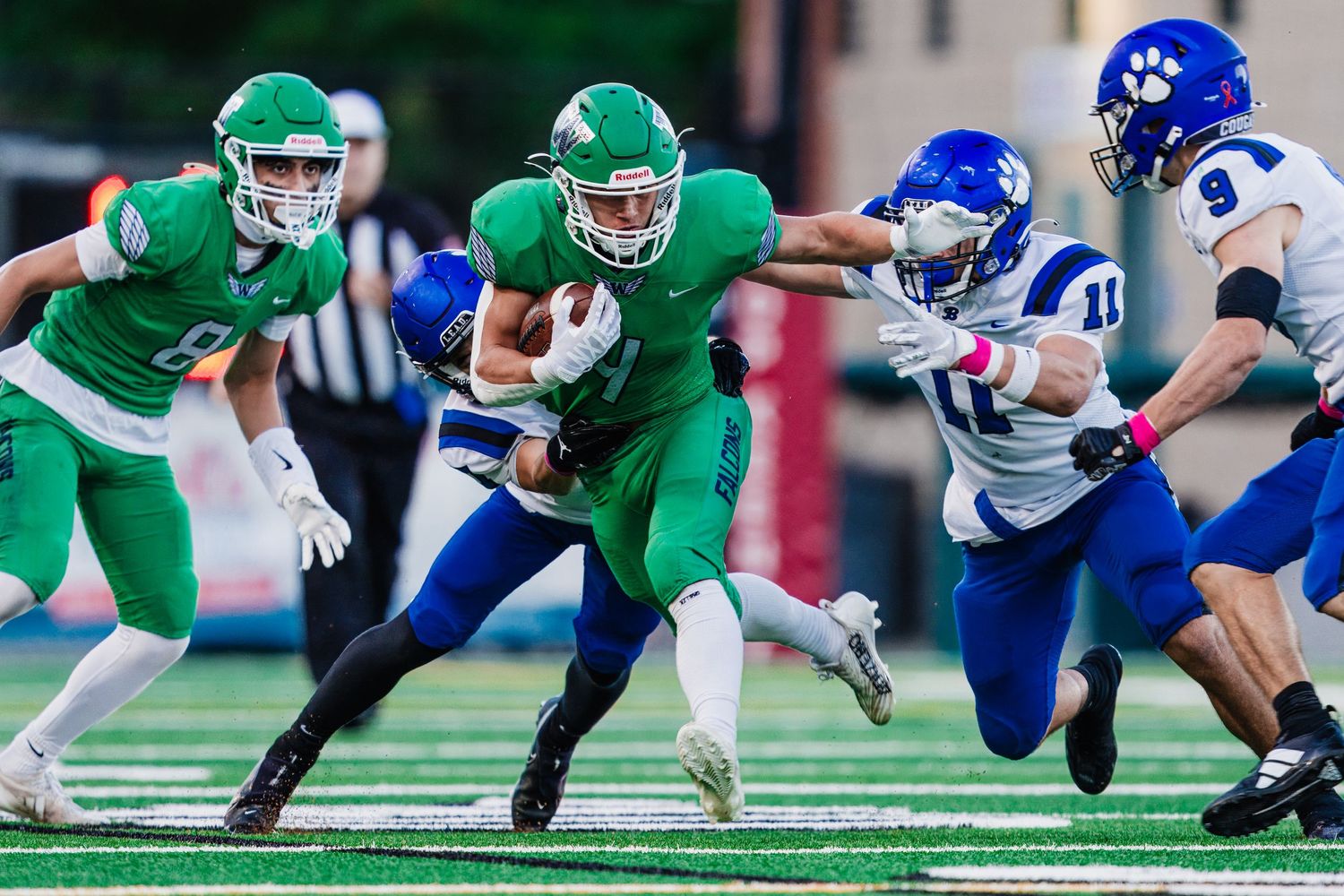 Football players in green and blue uniforms dive for the ball during an intense play on the field.